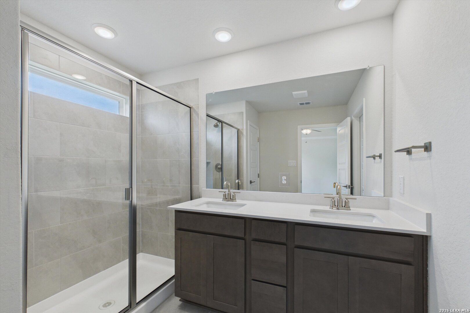Modern bathroom with double vanity, quartz countertop, and walk-in glass shower in The Charlotte B at Meadows at Oak Creek.
