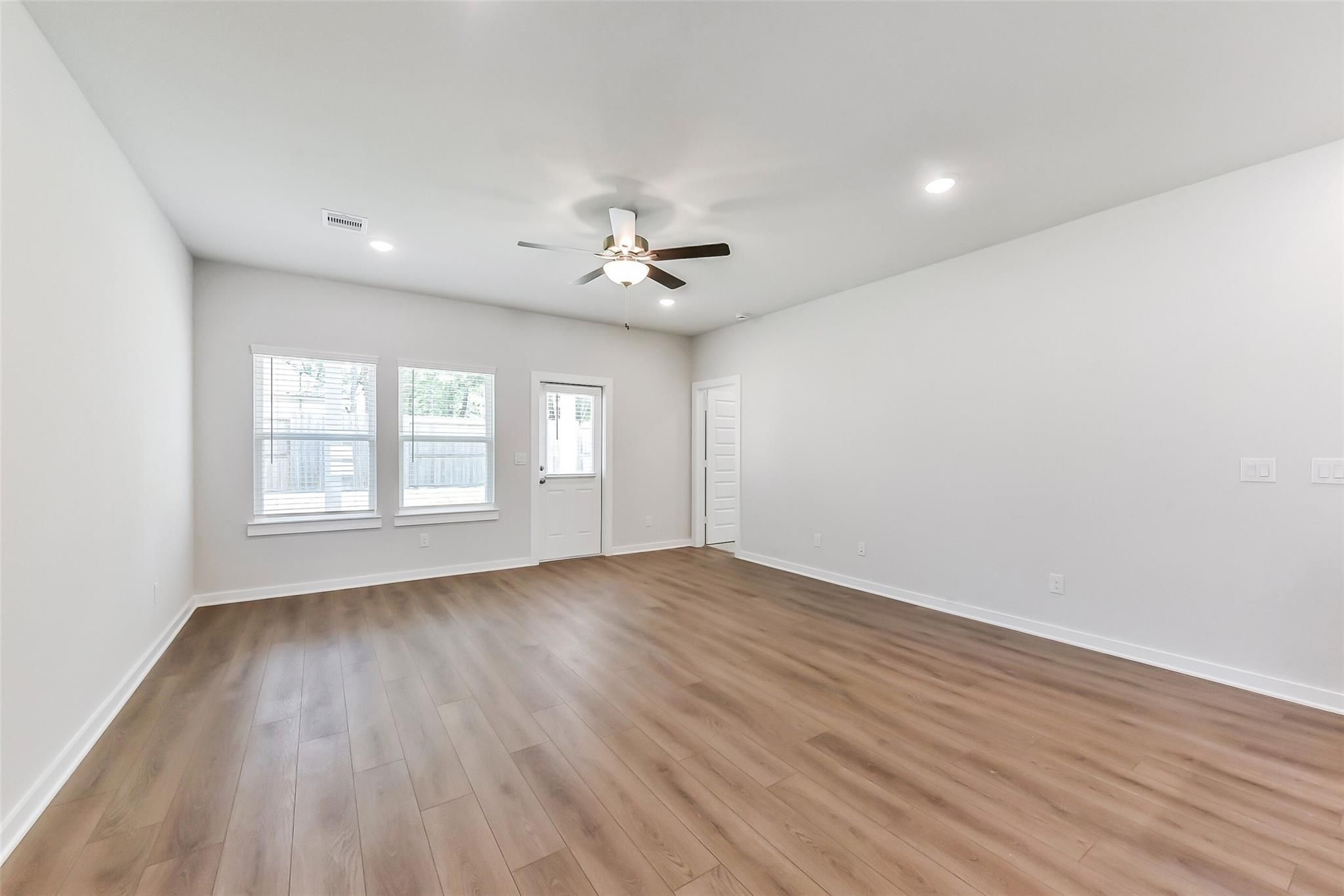 Bright living room with ceiling fan, large windows, French doors, and hardwood floors in Davidson Homes The Brazos E, Magnolia, Texas