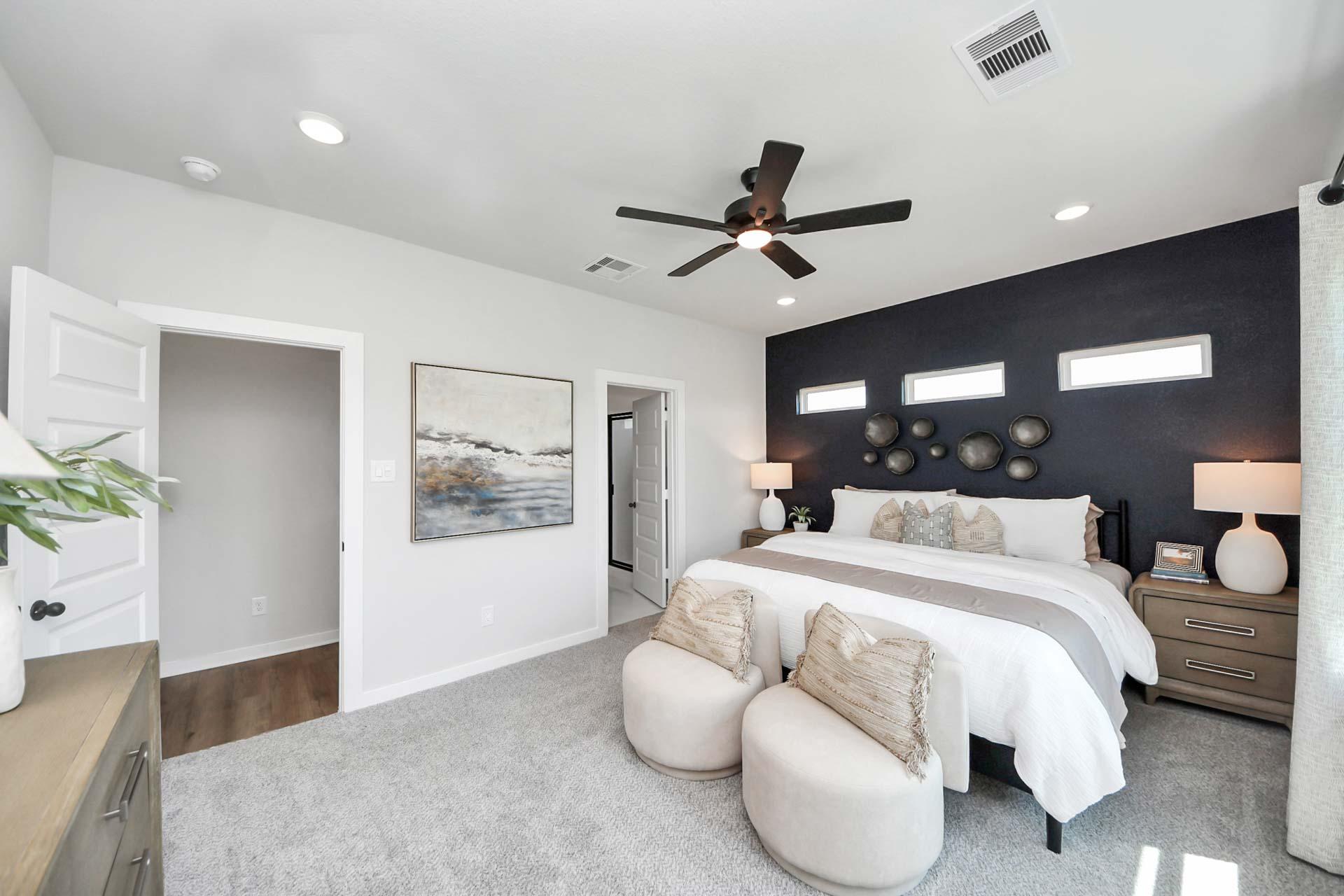Spacious primary bedroom at Enclave at Newport in Crosby, TX by Davidson Homes with dark accent wall and plush seating.