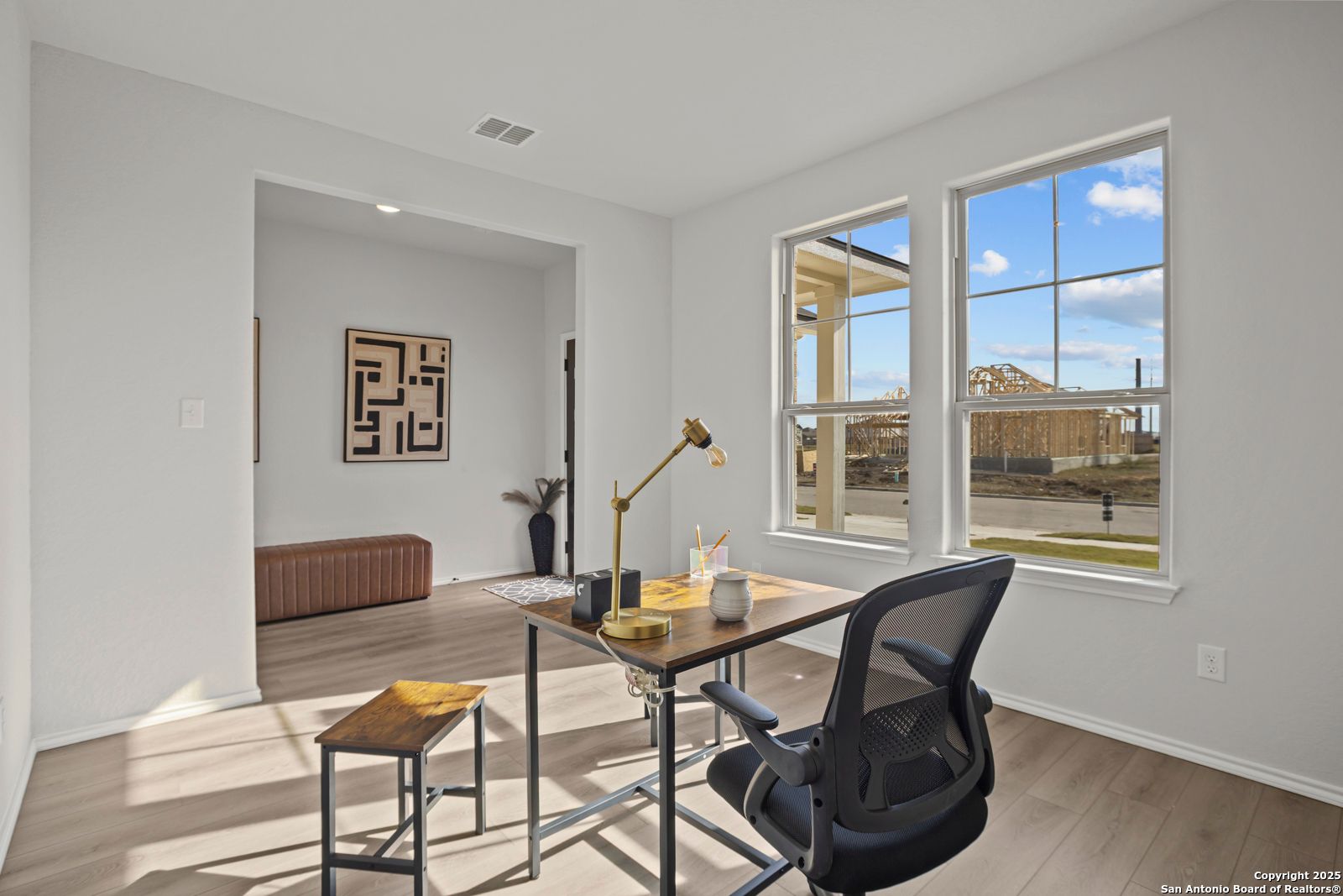 Modern home office with wooden desk, ergonomic chair, abstract wall art, and large windows in Davidson Homes The Douglas C, Seguin, Texas