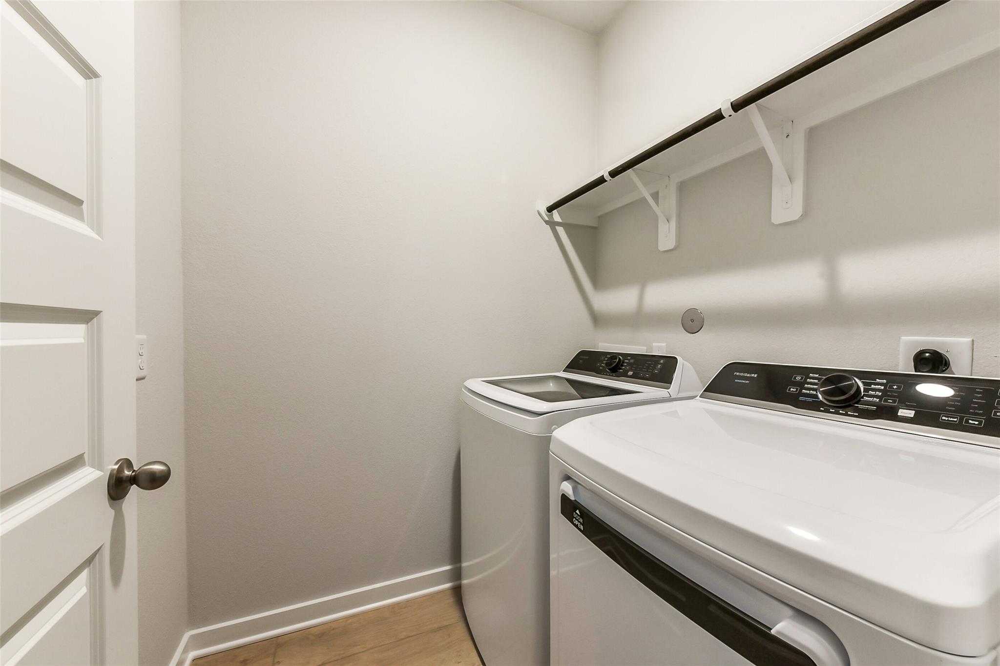 Modern laundry room featuring white washer, dryer, and open shelves in Davidson Homes The Laguna B, Sunterra, Katy, Texas