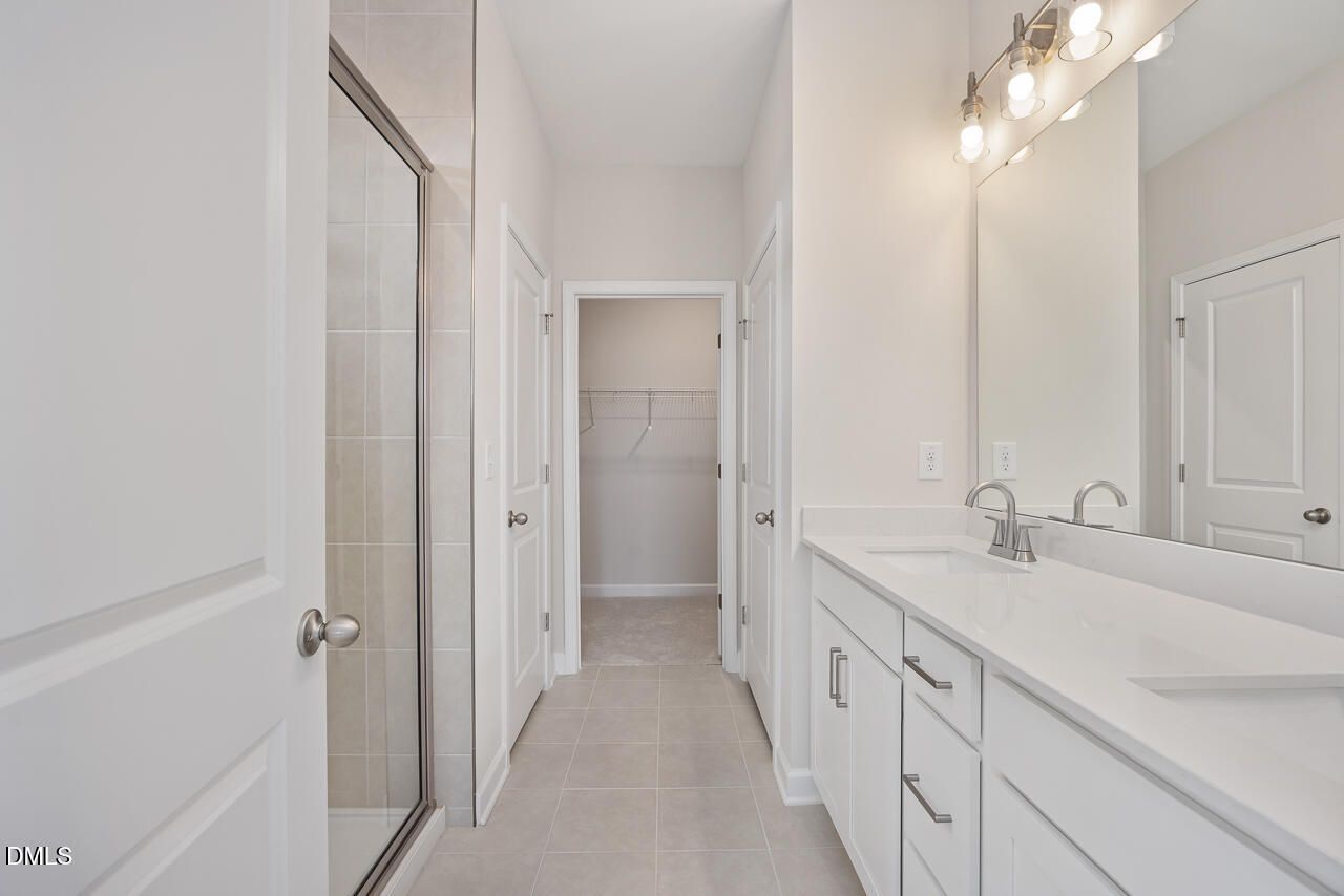 Modern master bathroom with glass shower, double vanity, and lighted mirror in The Daphne C by Davidson Homes, Lillington, NC