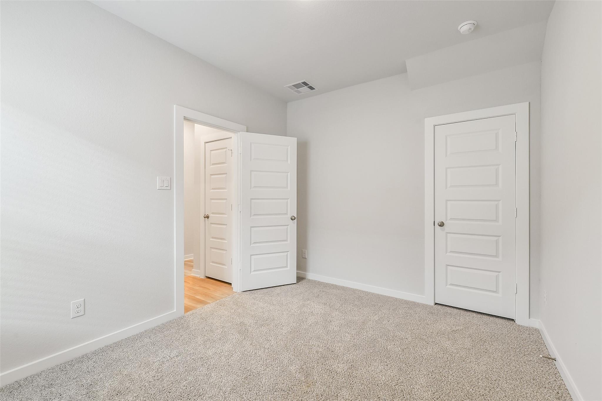 Empty bedroom featuring light gray walls, beige carpet flooring, open door to en-suite bathroom, and closet in Davidson Homes San Marcos E, Conroe Texas