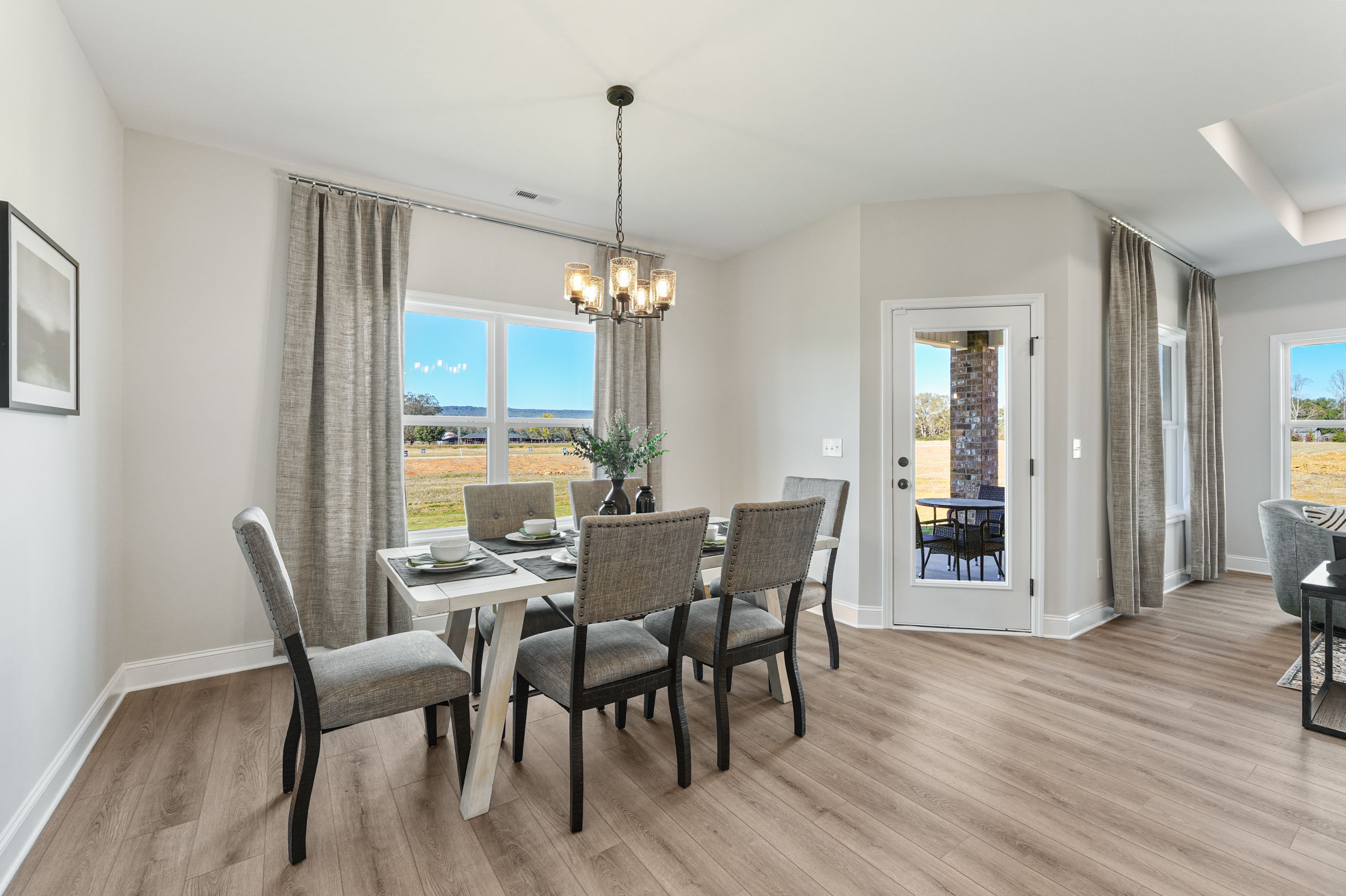 Modern dining room in Ramsay Cove Owens Cross Roads AL by Davidson Homes with gray chairs chandelier large windows and field views