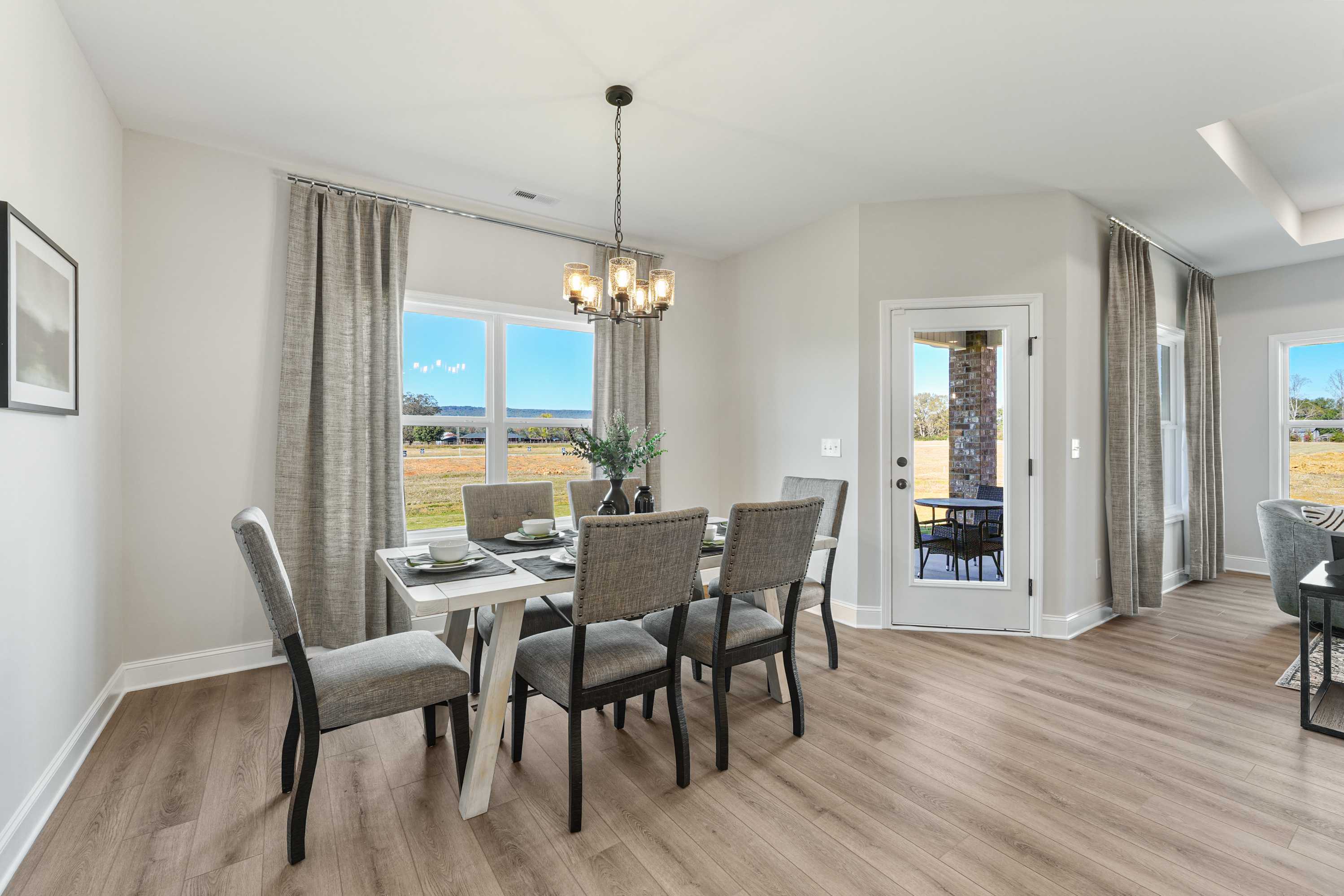 Modern dining room in Ramsay Cove Owens Cross Roads AL by Davidson Homes with gray chairs chandelier large windows and field views