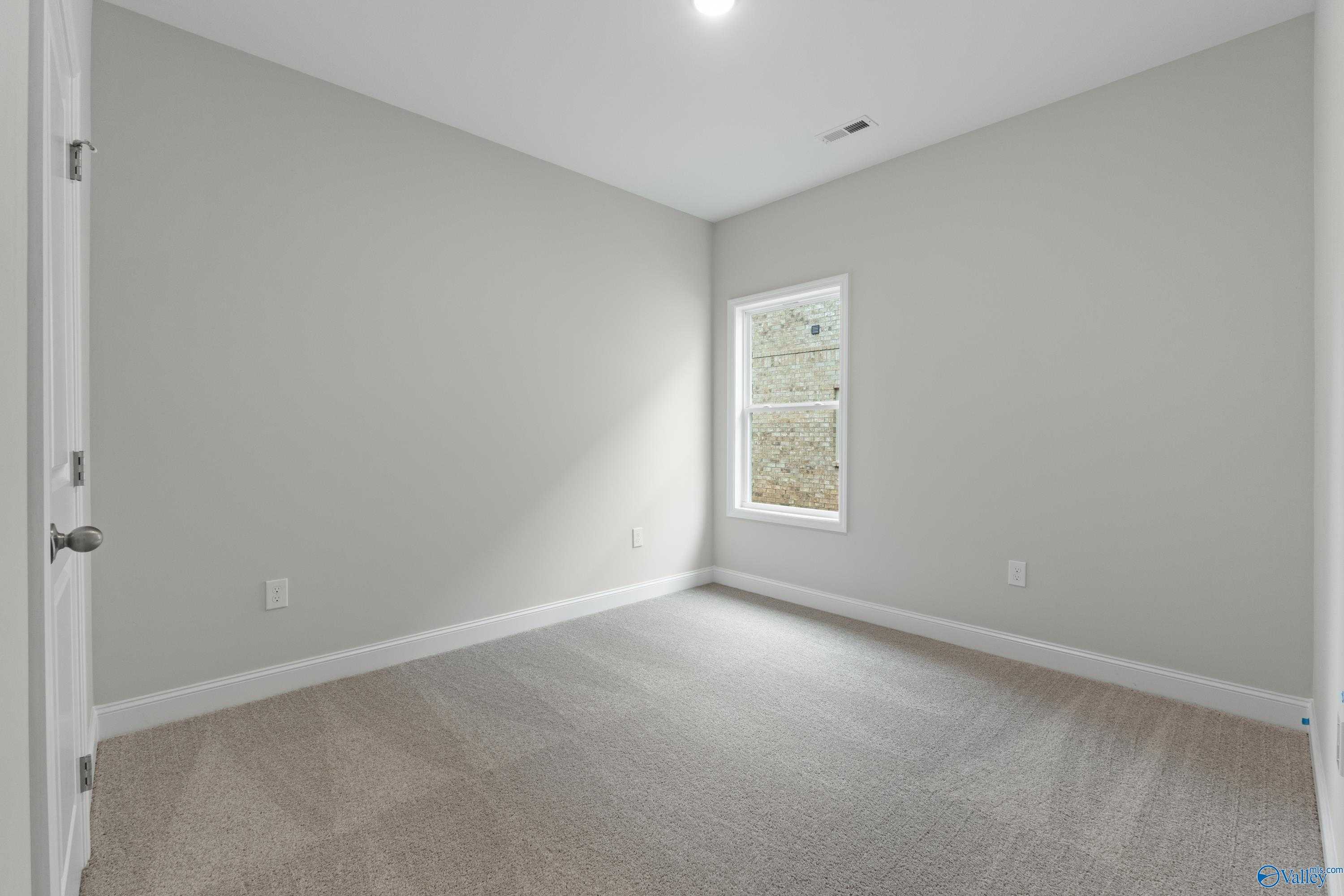 Empty secondary bedroom featuring light gray walls, large window with blinds, and neutral carpet in Davidson Homes The Asheville C, Huntsville AL