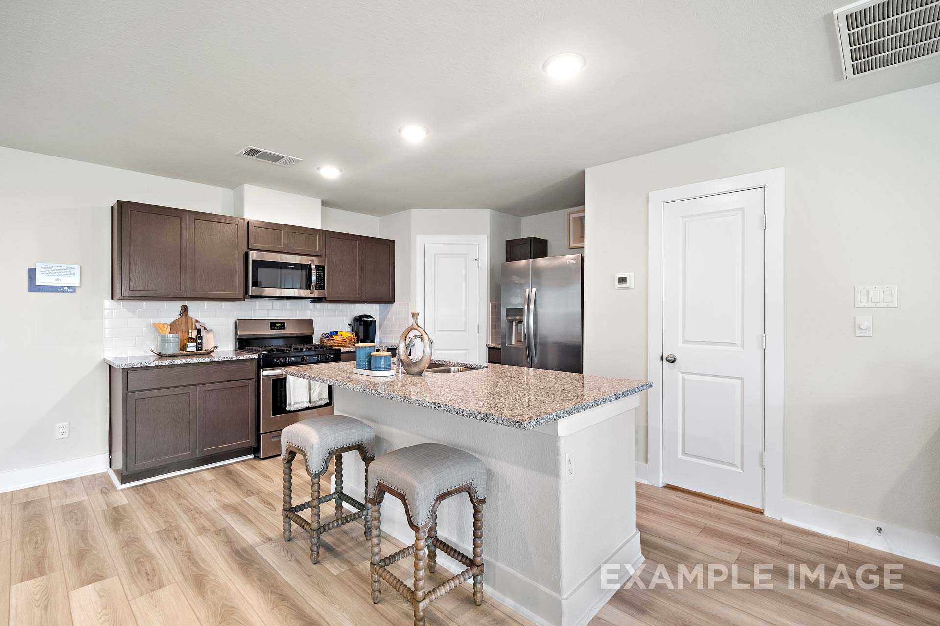 Modern kitchen in The Lily A home design with dark cabinets, granite island, stainless steel appliances, Cypress TX