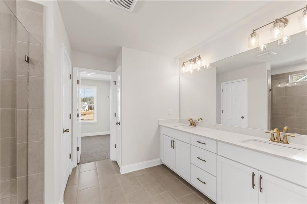 Modern master bathroom featuring double vanity with gold faucets, large mirror, and tiled walk-in shower in Davidson Homes The Willow B, Hoschton, GA