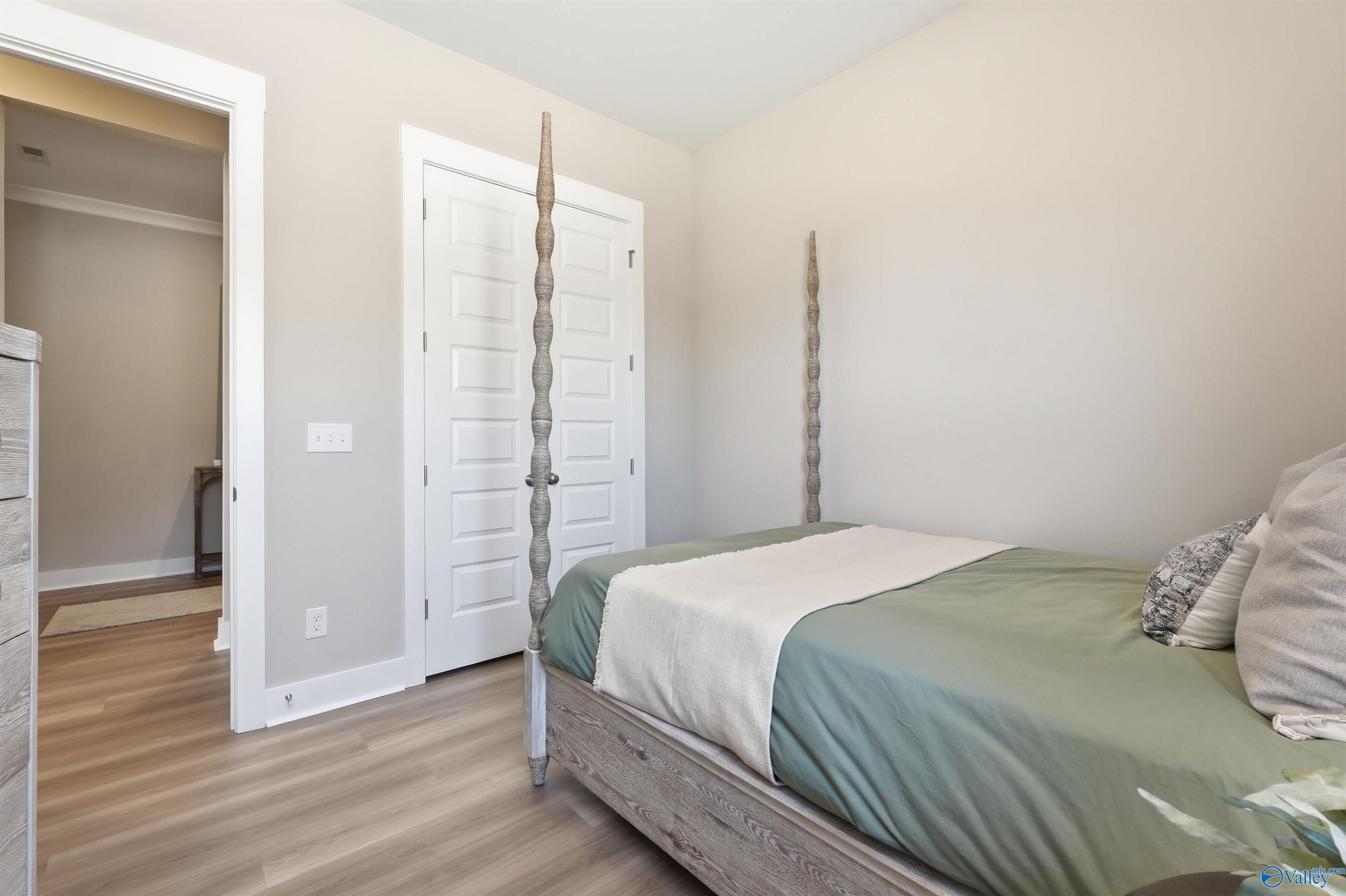 Cozy secondary bedroom featuring four-poster bed with green duvet, white closet doors, and light wood floors in Evermore Homes The Oxford B, Owens Cross Roads