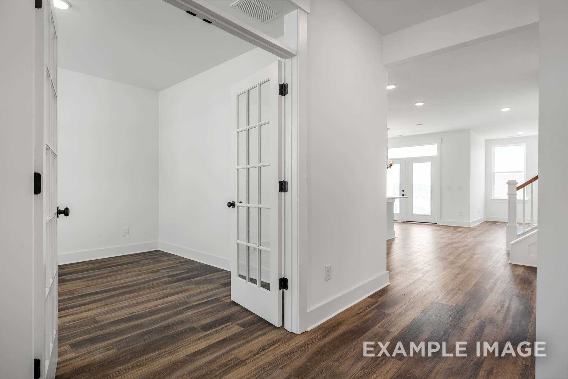Open-concept main floor study with French doors, hardwood floors, and hallway to living area in The Ash C home design