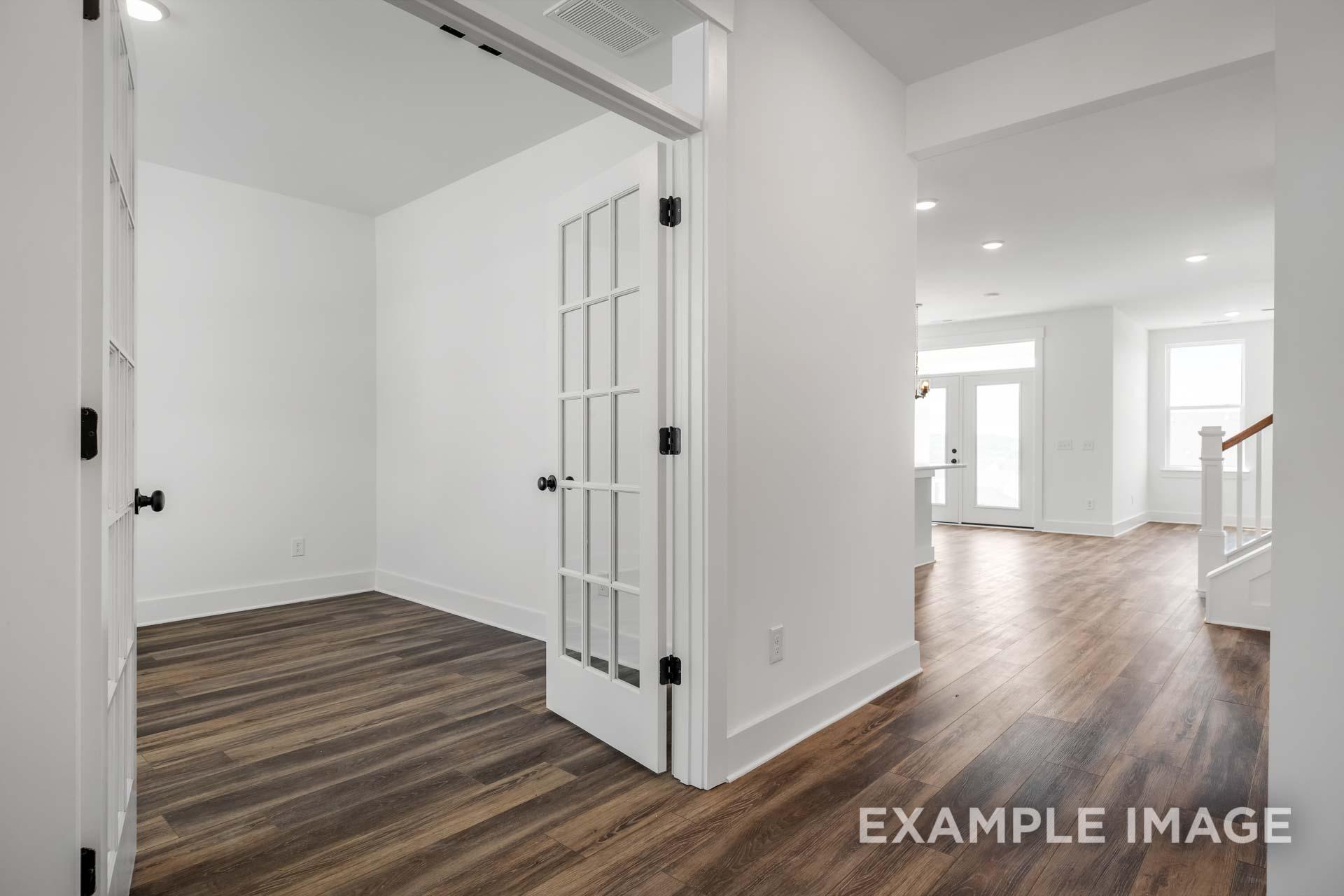 Open-concept main floor study with French doors, hardwood floors, and hallway to living area in The Ash C home design
