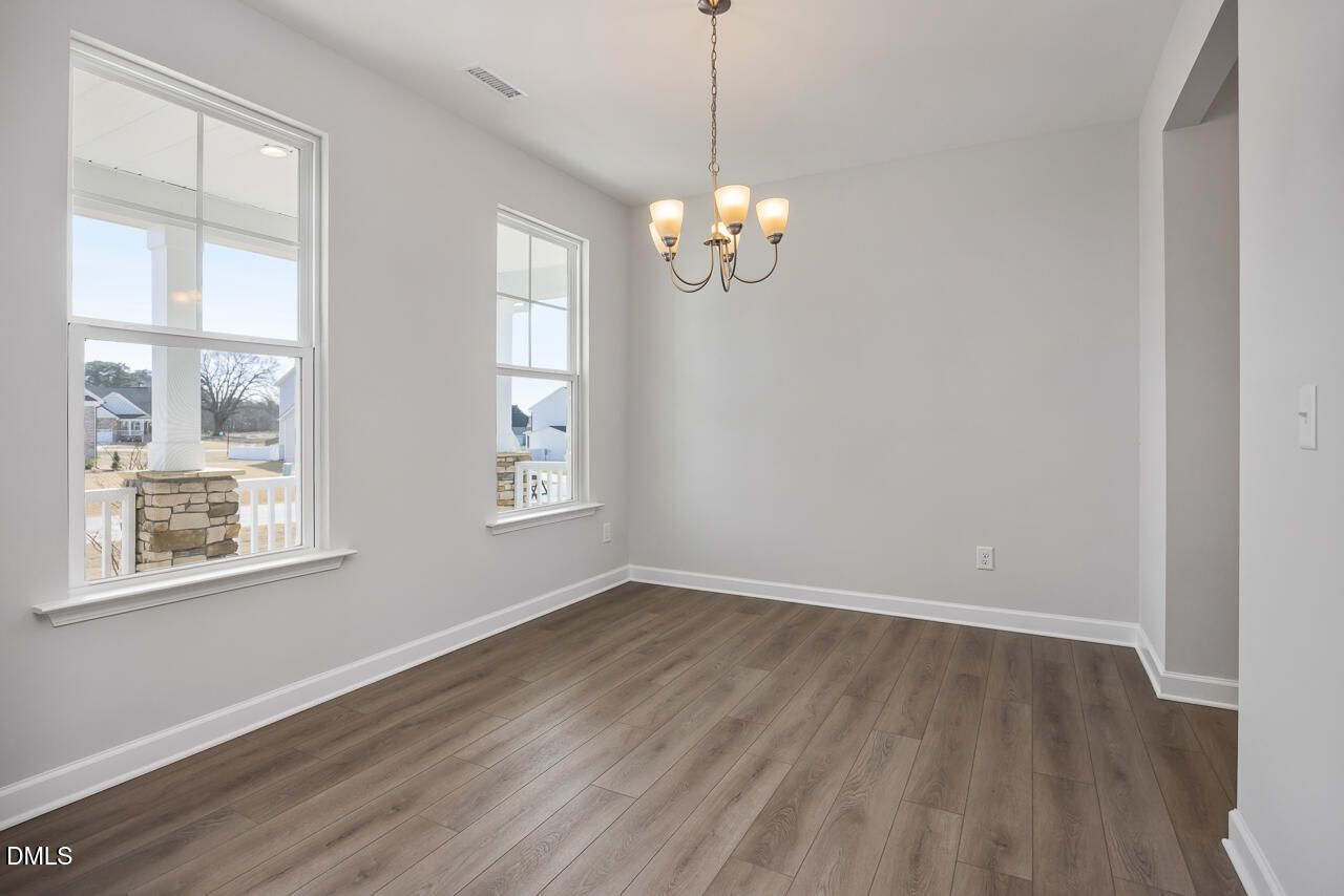 Bright dining room with hardwood floors, chandelier, and large windows overlooking porch in The Willow G home, Angier, NC