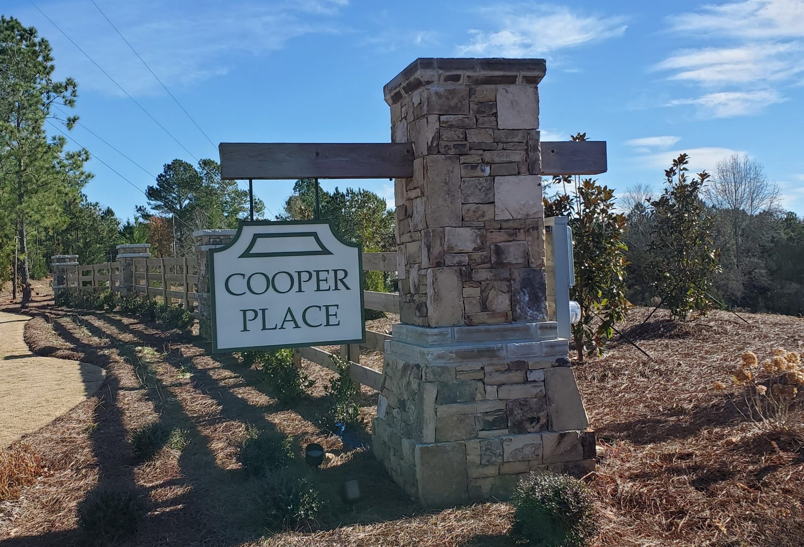 Cooper Place entrance sign in Cumming GA with stone pillars, wooden arch, pine trees, and fence