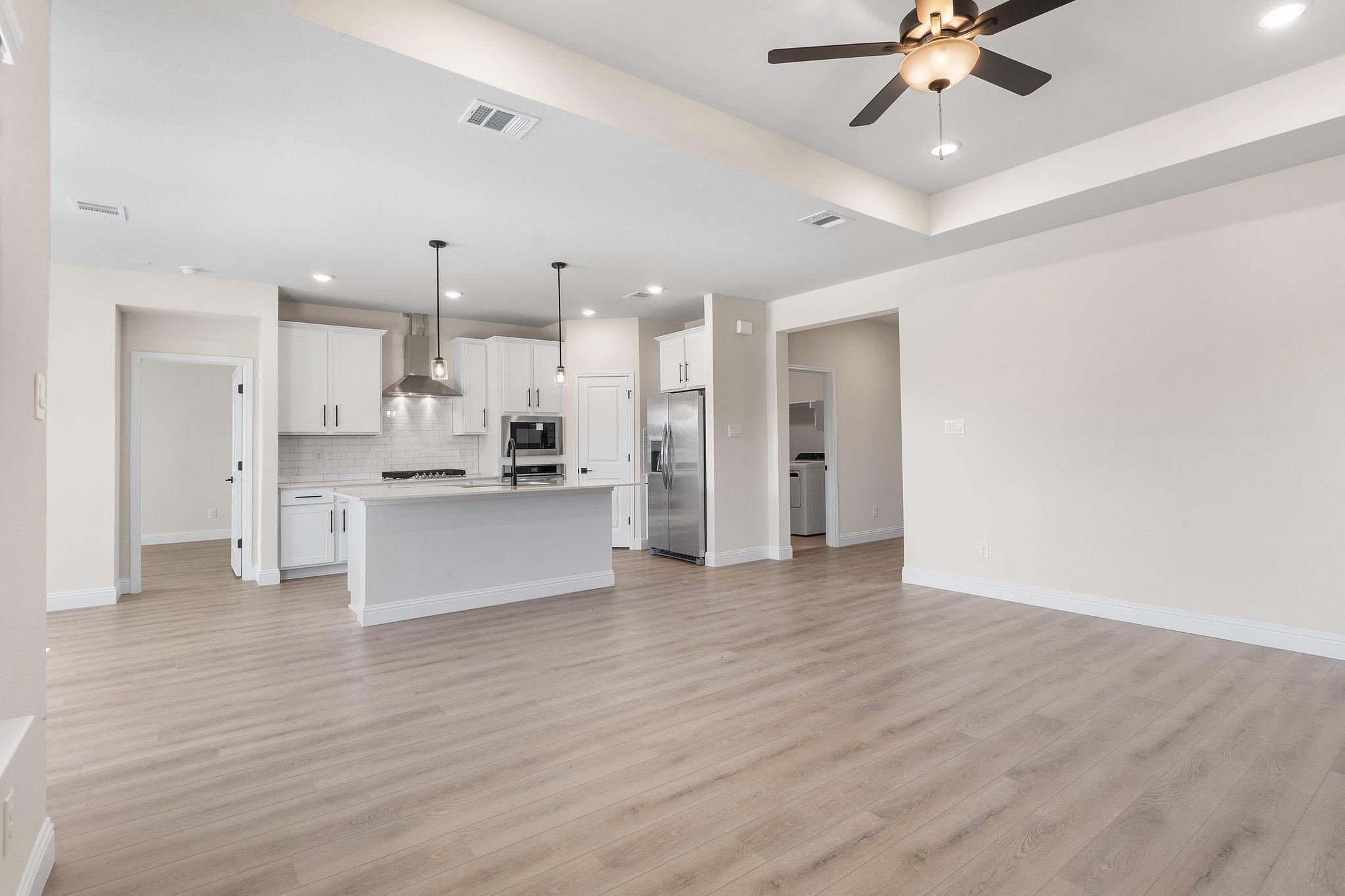 Open-concept kitchen and living area in The Holly F home design featuring white cabinetry, island, and wood-look flooring.