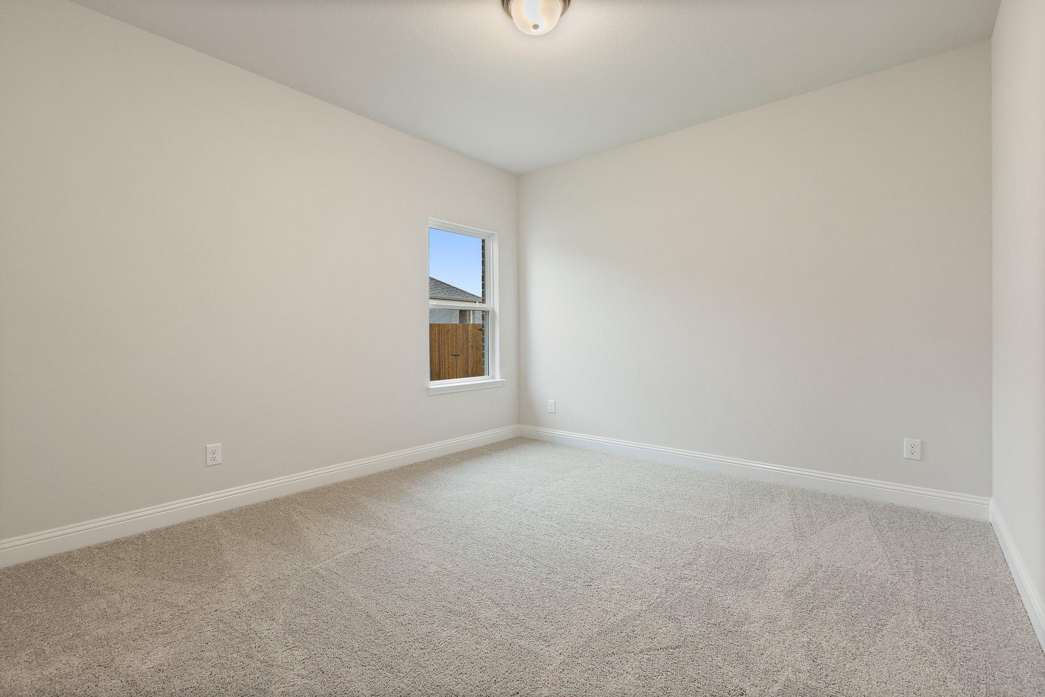 Spacious empty bedroom in The Harrison D home design with neutral walls, plush beige carpet, and window overlooking wooden fence