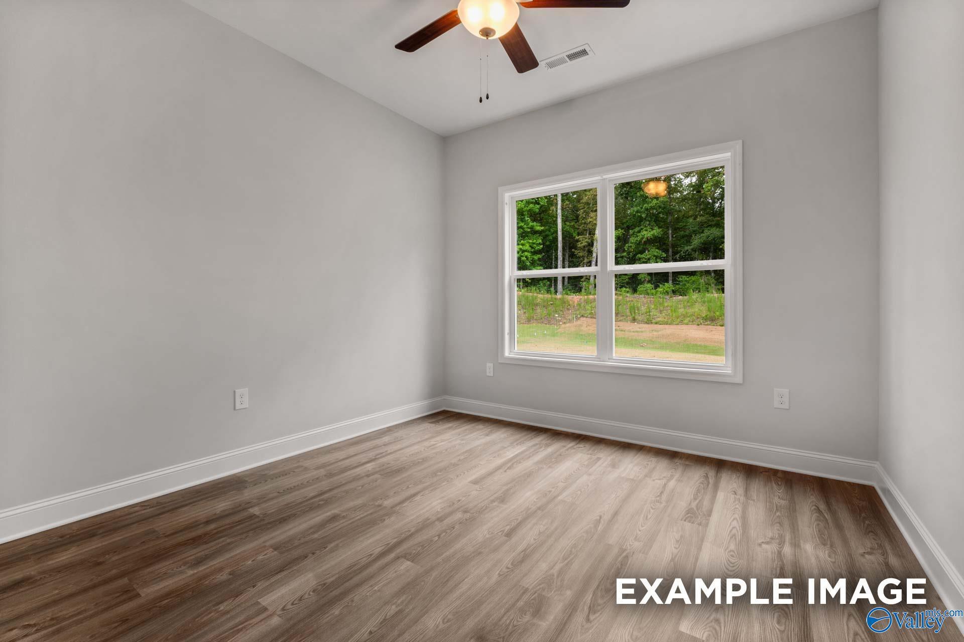 Bright bedroom featuring gray walls, hardwood floors, ceiling fan, and large window with wooded view in Davidson Homes The Shelby C, Arab, Alabama