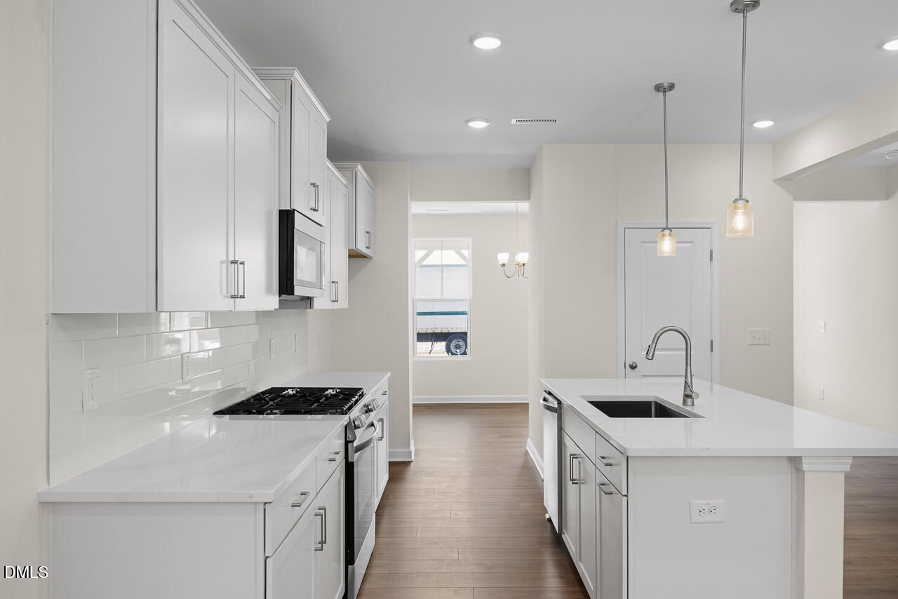White shaker kitchen with island, gas range, and subway tile backsplash in Davidson Homes The Willow B, Zebulon, North Carolina