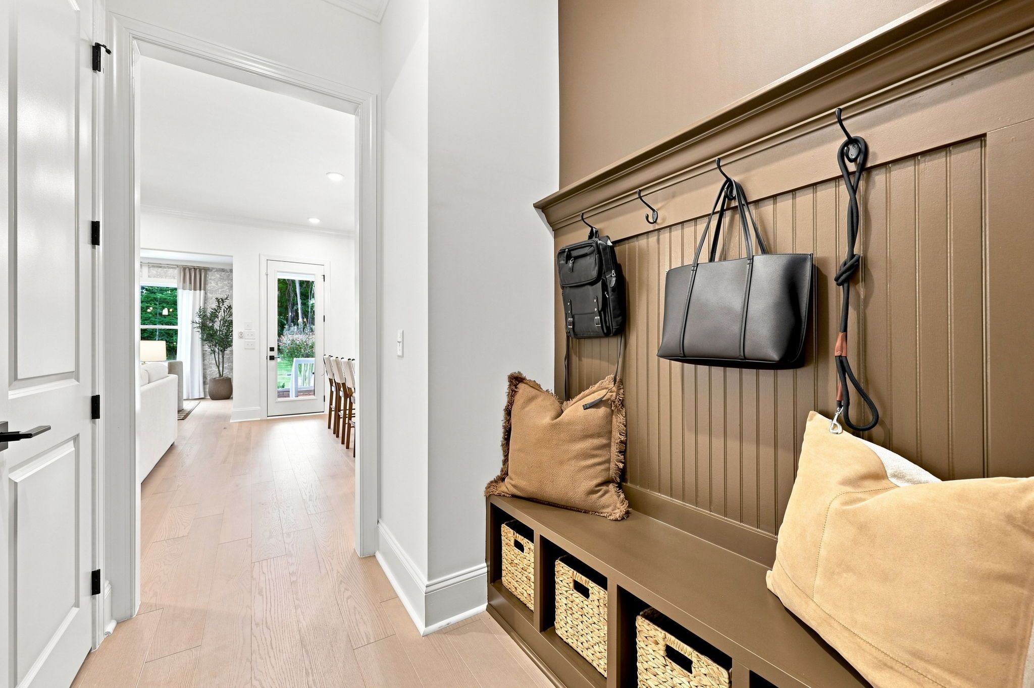 Mudroom drop zone in The Barrington C featuring built-in bench, wall hooks, and storage baskets with view of living area.