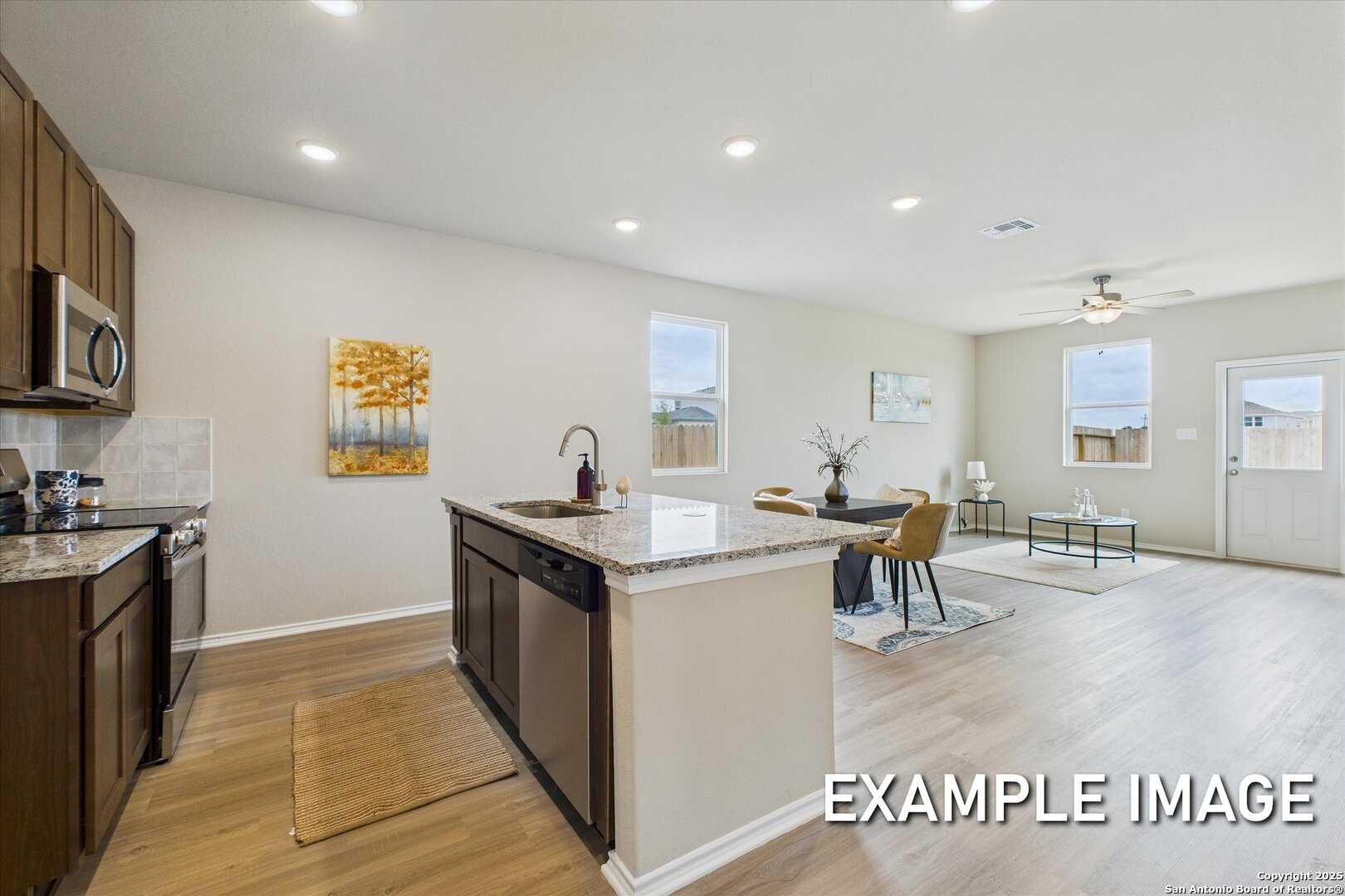 Open-concept kitchen with granite island, stainless appliances, and dark cabinets in Davidson Homes The Comal B, San Antonio