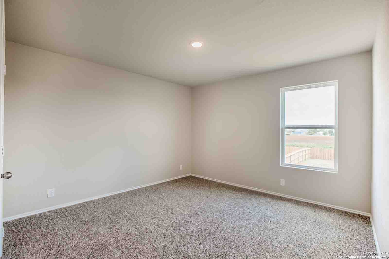 Bright empty bedroom with beige walls, carpeted floor, and large window in Davidson Homes The Murray H, Seguin, Texas