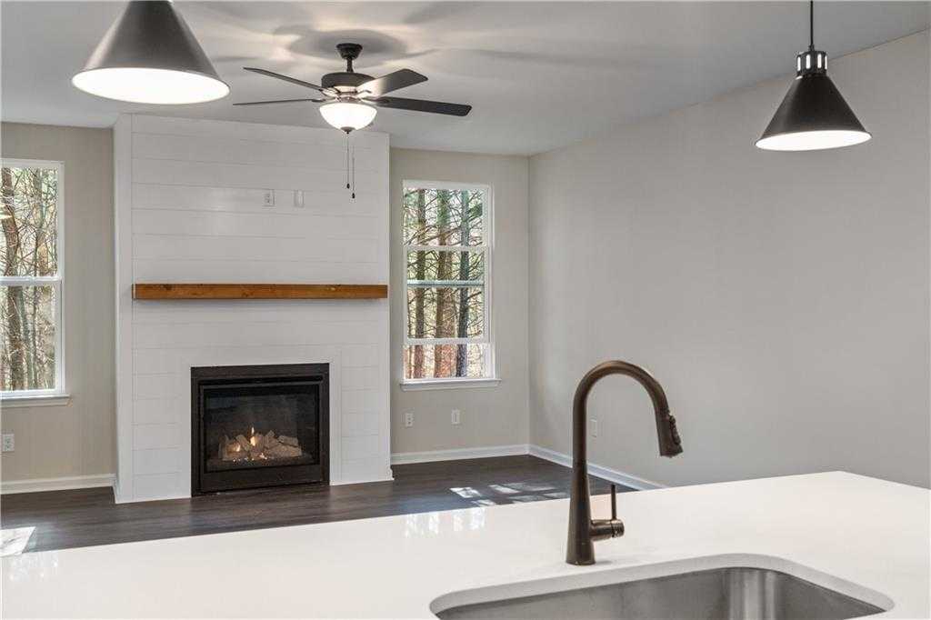 Open-concept living room with shiplap gas fireplace, kitchen island sink, and wooded views in Davidson Homes The Daphne B, Loganville, GA