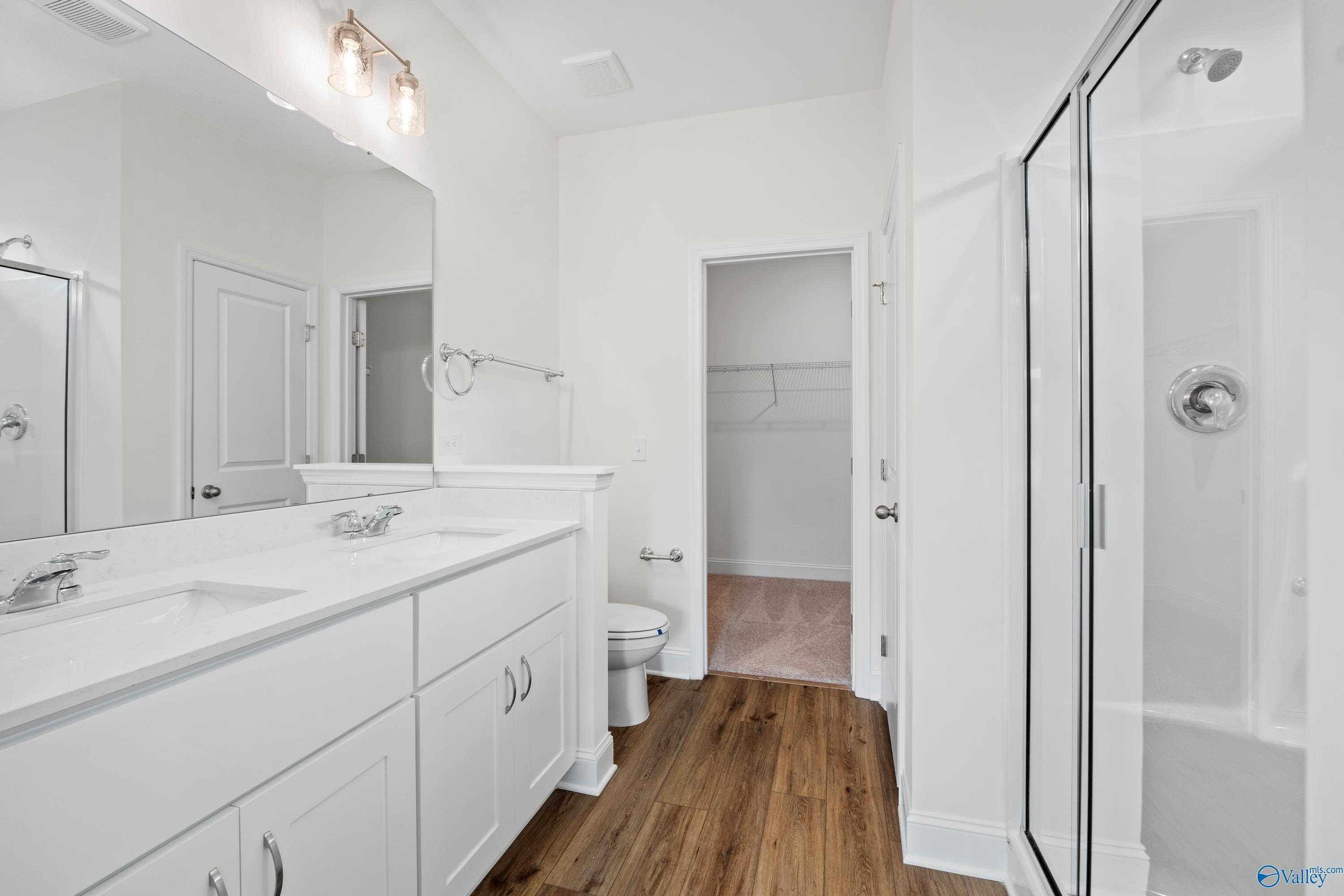 Modern master bathroom with double white vanity, large mirror, glass shower, and linen closet in Davidson Homes The Asheville C, Athens, AL