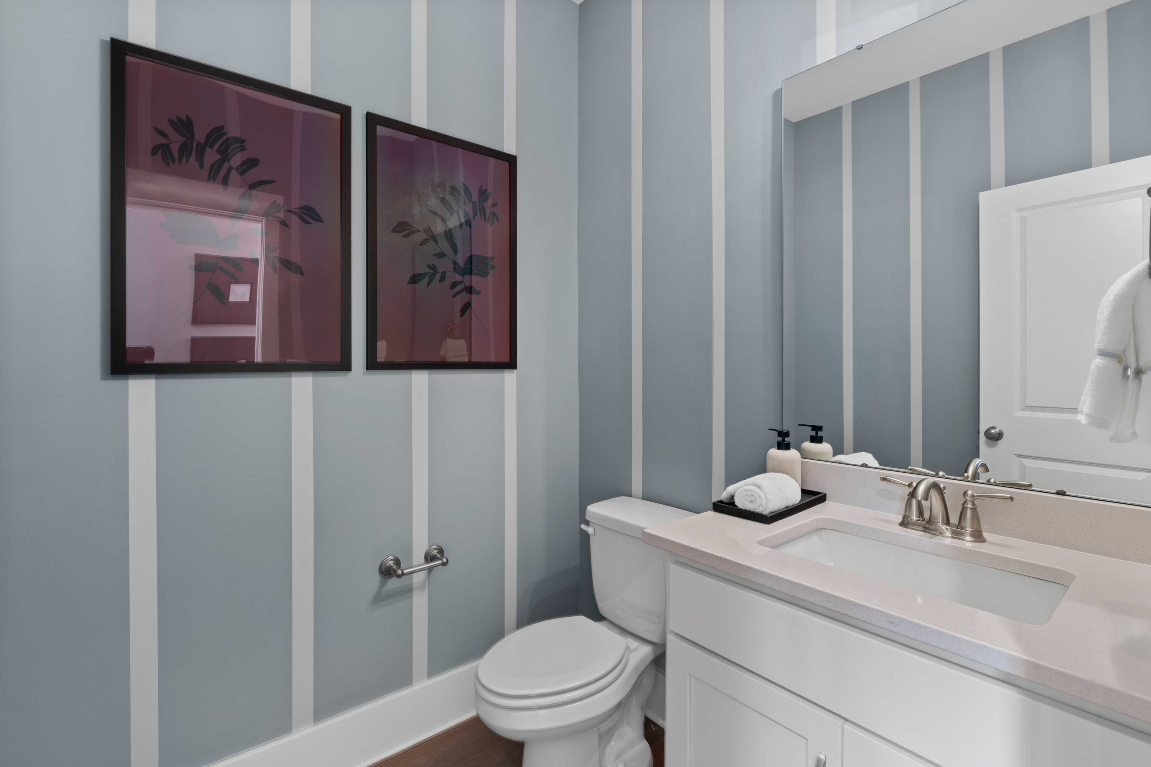 Modern powder room at Creekside in Harvest Alabama with blue striped walls, abstract framed artwork, white vanity sink, and toilet