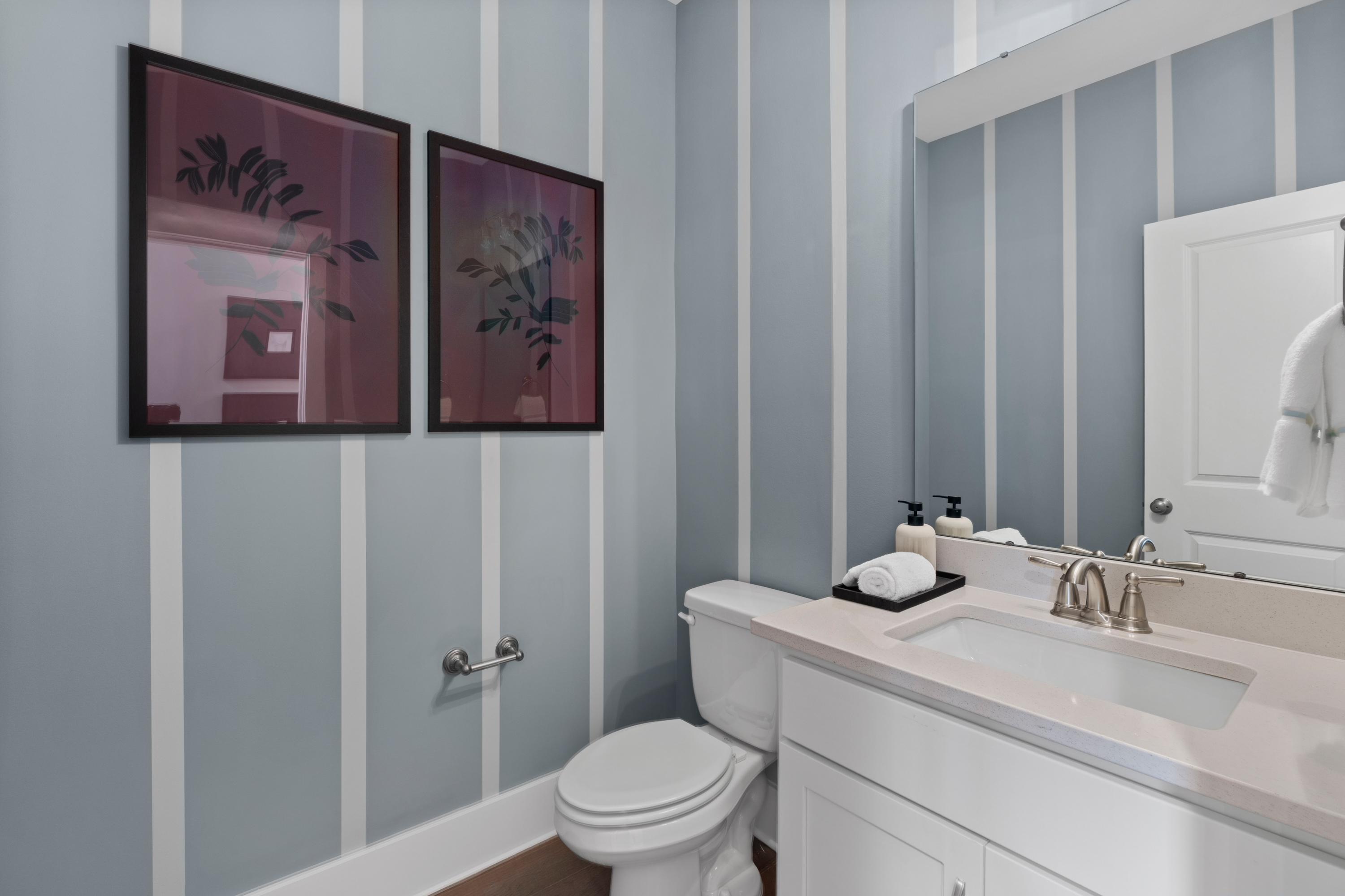Modern powder room at Creekside in Harvest Alabama with blue striped walls, abstract framed artwork, white vanity sink, and toilet