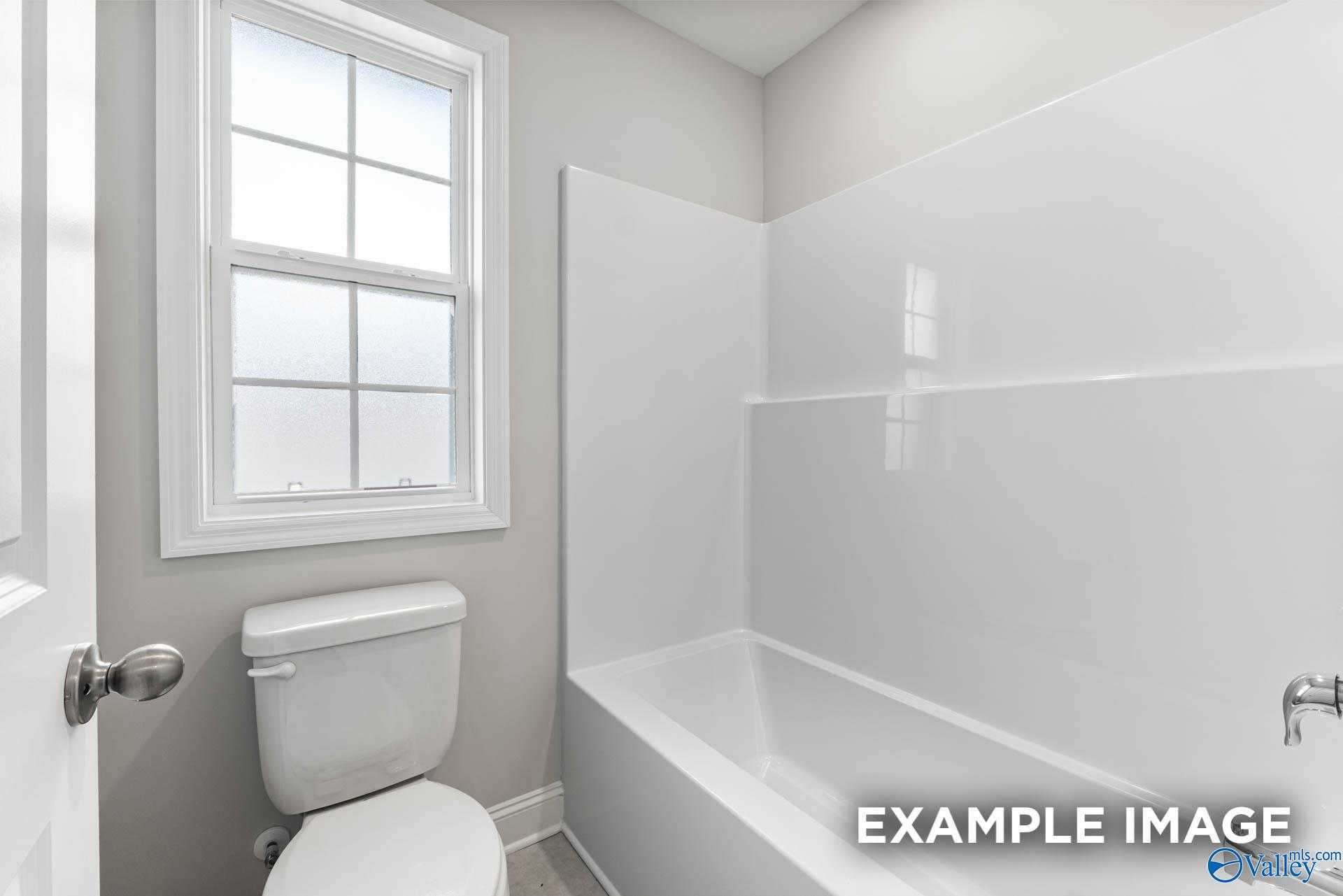 Bright bathroom with white tub, shower enclosure, toilet, and frosted window in Davidson Homes The Madison A, Harvest, Alabama