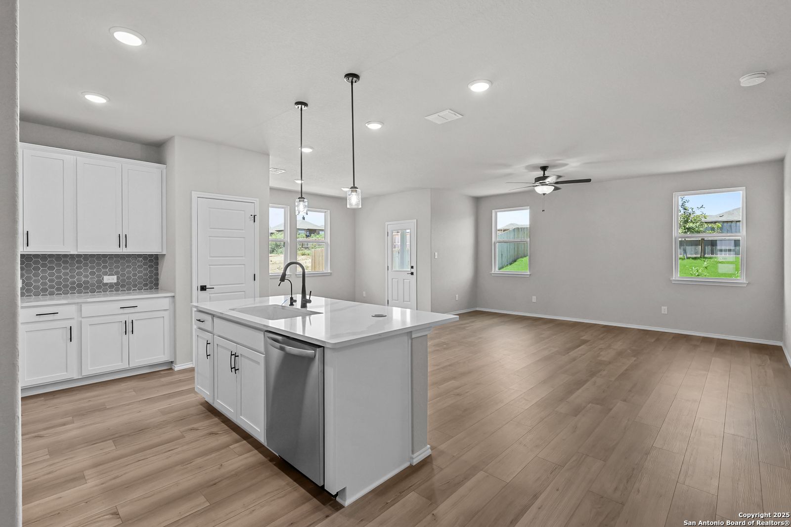 Modern open-concept kitchen with white cabinets, quartz island sink, and hardwood floors in The Daphne K, San Antonio