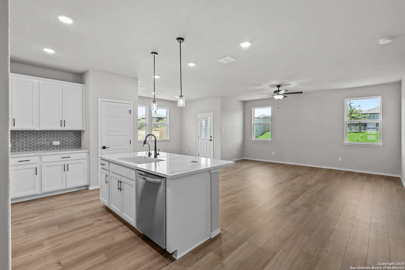 Modern open-concept kitchen with white cabinets, quartz island sink, and hardwood floors in The Daphne K, San Antonio