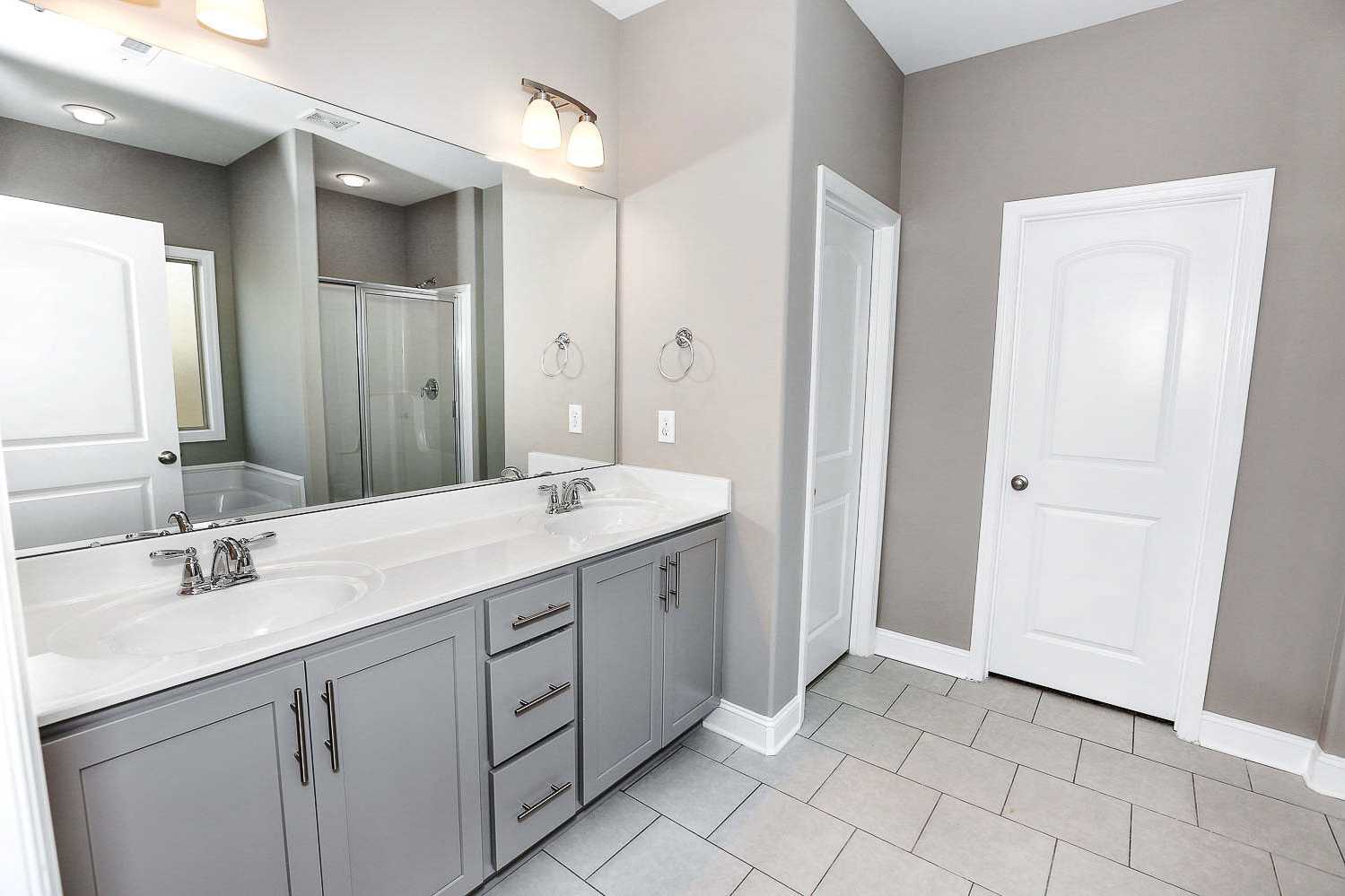 Spacious master bathroom in The Montgomery by Davidson Homes featuring double gray vanity, large mirror, walk-in shower, and tiled floor