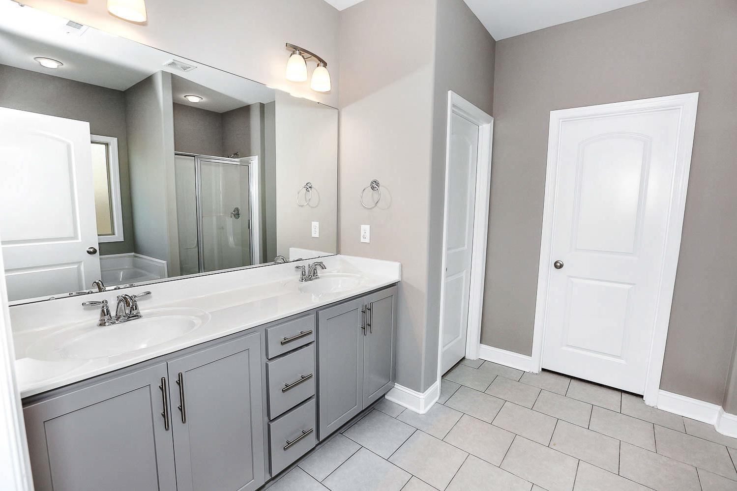 Spacious master bathroom in The Montgomery by Davidson Homes featuring double gray vanity, large mirror, walk-in shower, and tiled floor