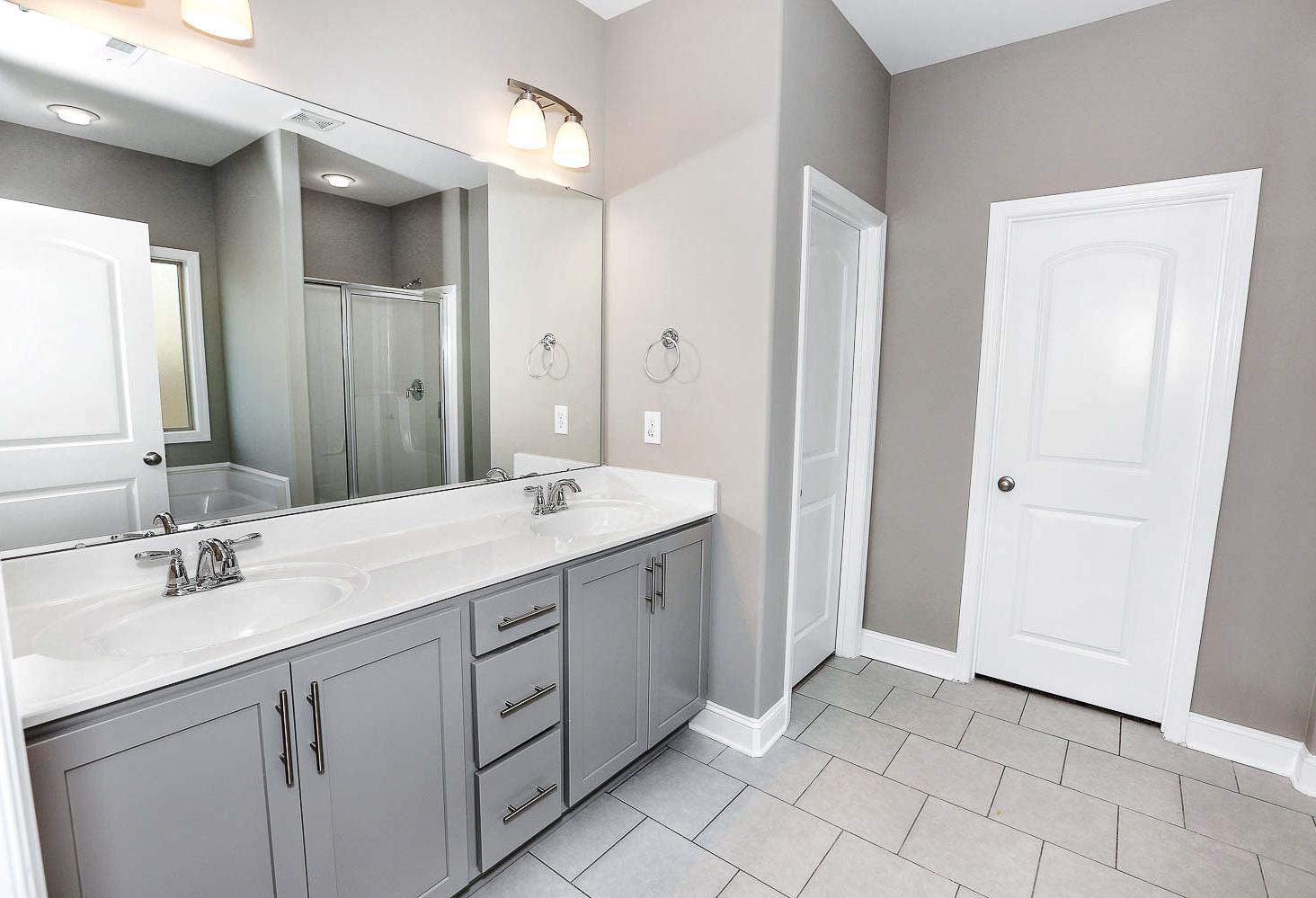 Spacious master bathroom in The Montgomery by Davidson Homes featuring double gray vanity, large mirror, walk-in shower, and tiled floor