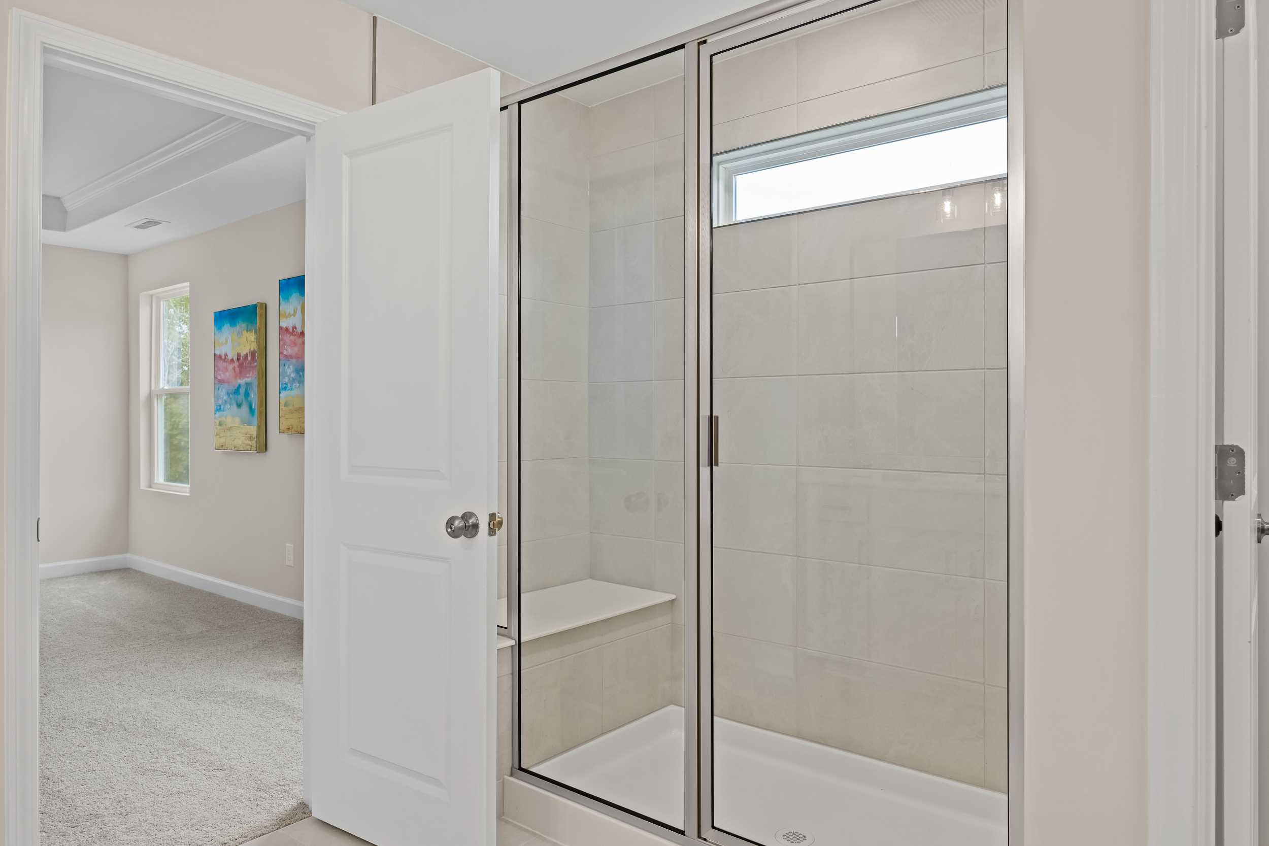 Modern primary bathroom at Gregory Village in Lillington NC with frameless glass shower, built-in bench, and subway tile walls