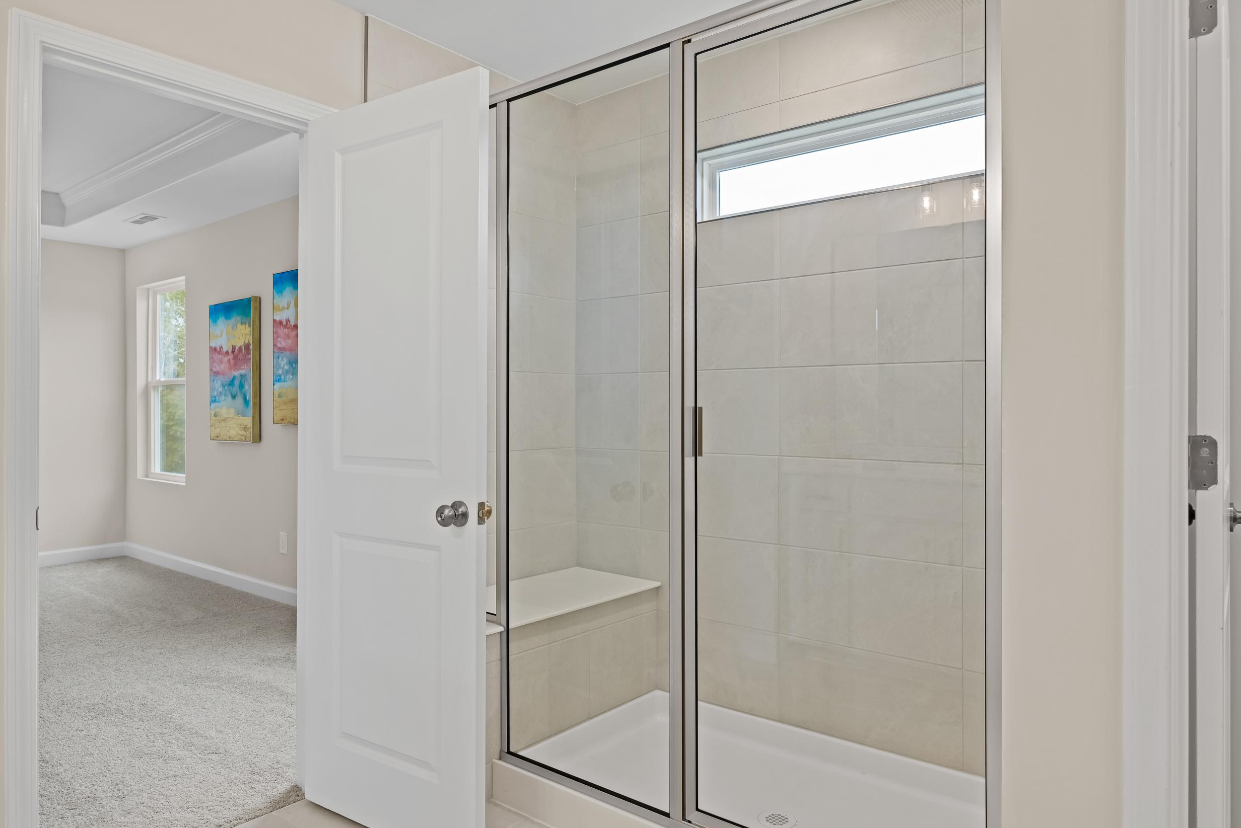 Modern primary bathroom at Gregory Village in Lillington NC with frameless glass shower, built-in bench, and subway tile walls