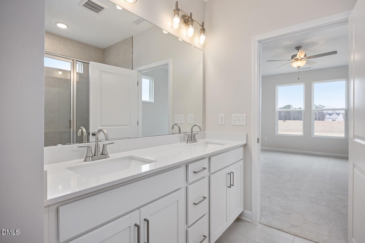 Elegant master bathroom with double white quartz vanity, glass shower, and adjacent carpeted bedroom in Davidson Homes The Daphne C, Lillington NC