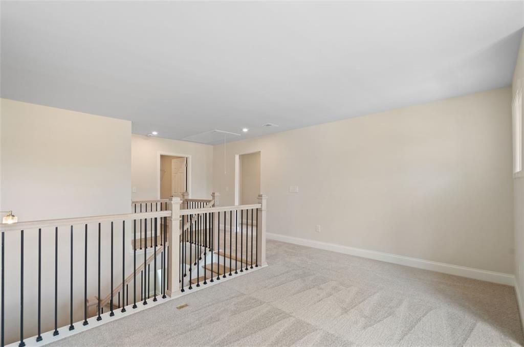 Open upstairs hallway with black iron railings, hardwood floors, and recessed lights in Davidson Homes The Willow D at Wehunt Meadows, Hoschton