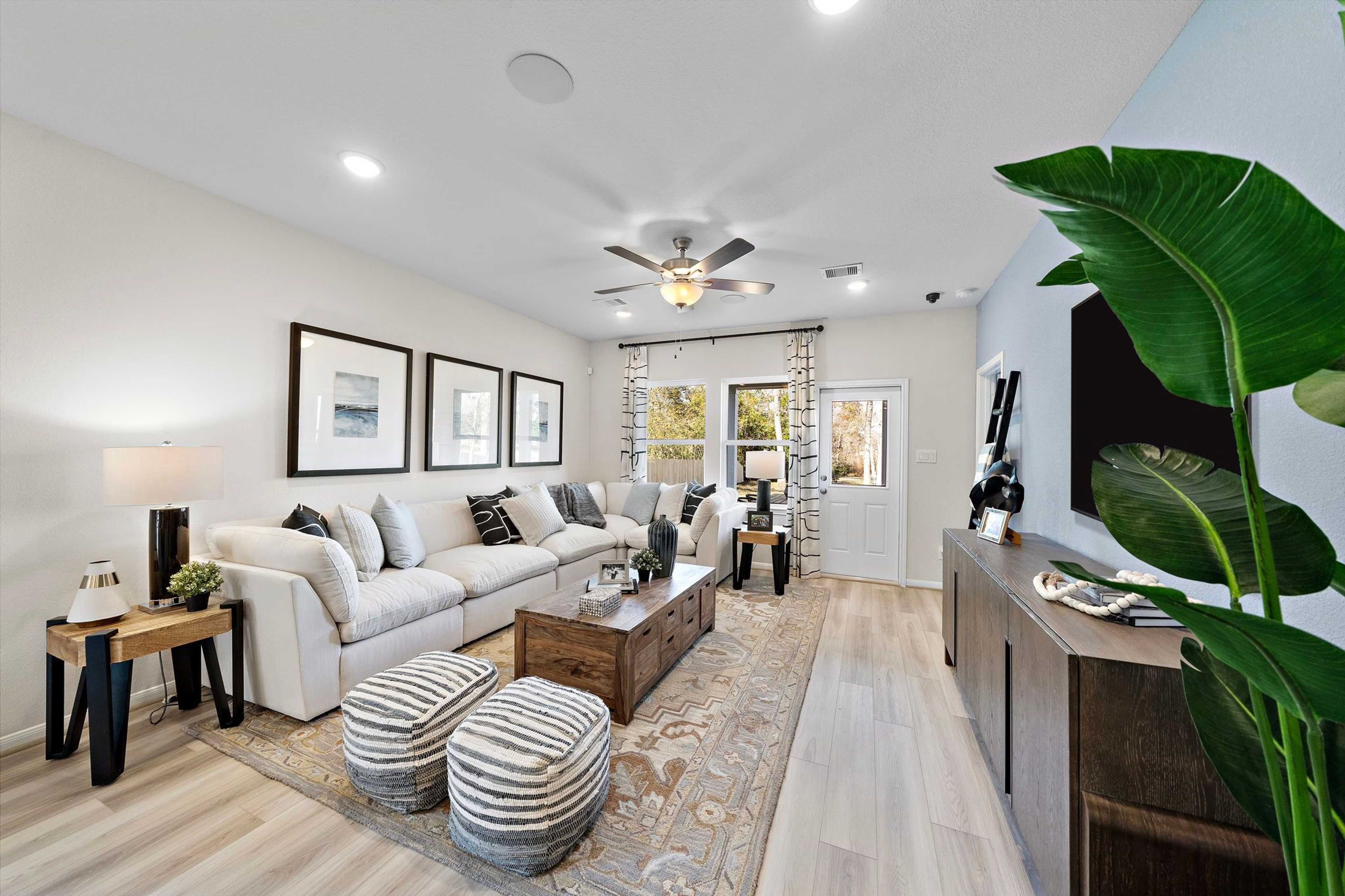 Spacious open-concept living room in Heartland Texas Davidson Homes with white L-shaped sofa, hardwood floors, ceiling fan, and potted plants