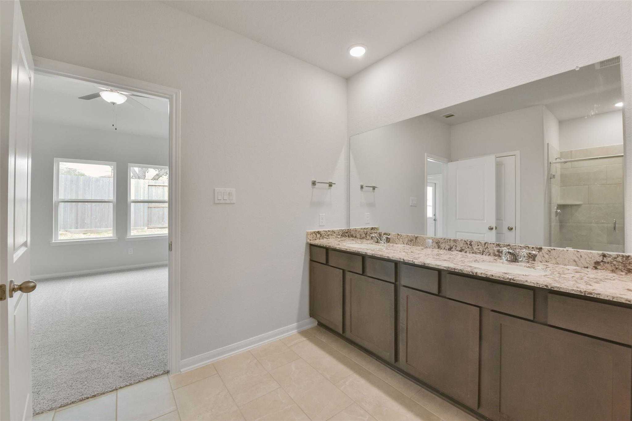 Modern master bathroom featuring double vanity, granite countertop, large mirror, and glass shower in Davidson Homes The Laguna B, Magnolia, Texas