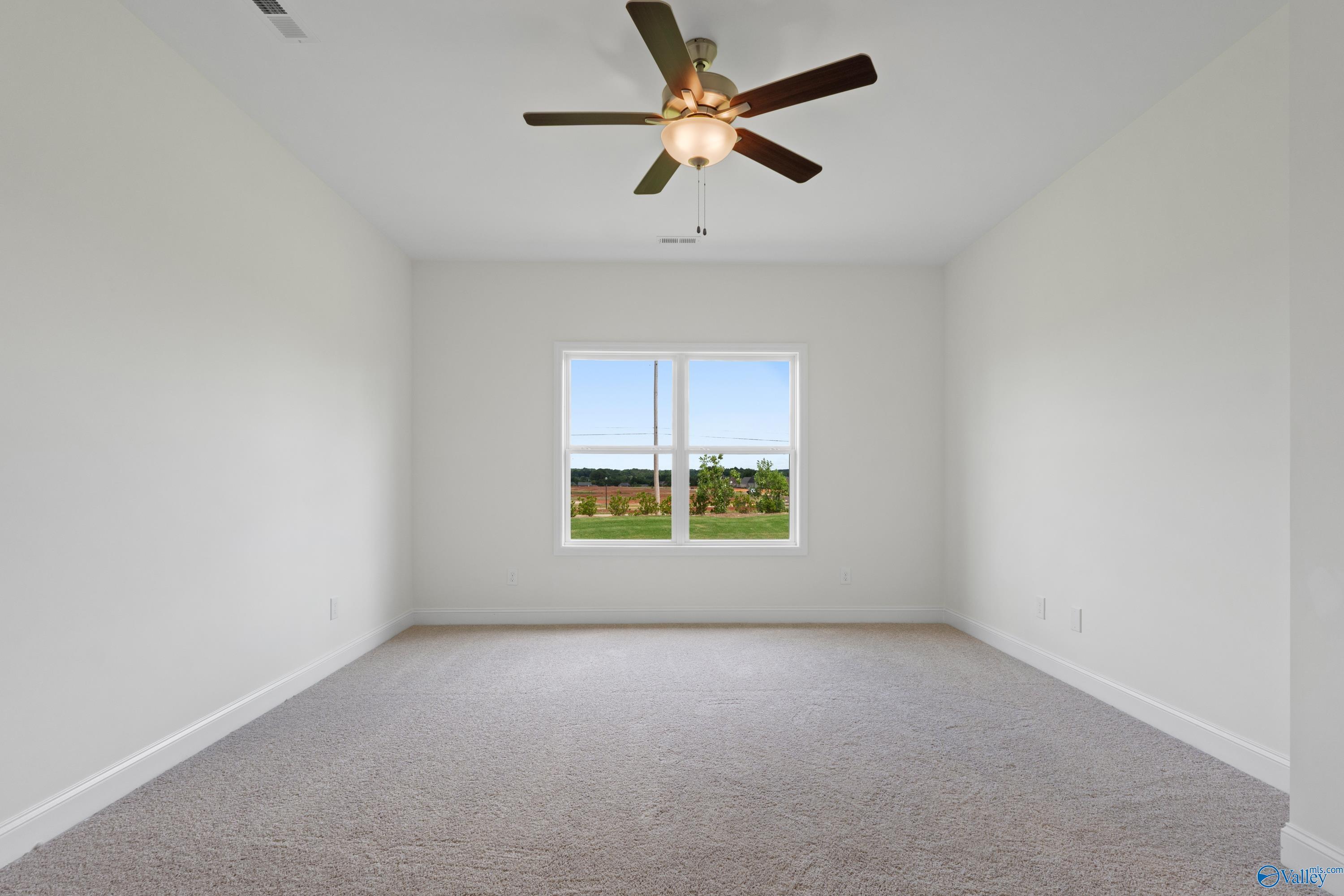 Spacious bedroom with neutral carpet and ceiling fan in The Everett B floor plan at The Meadows in Athens, Alabama.