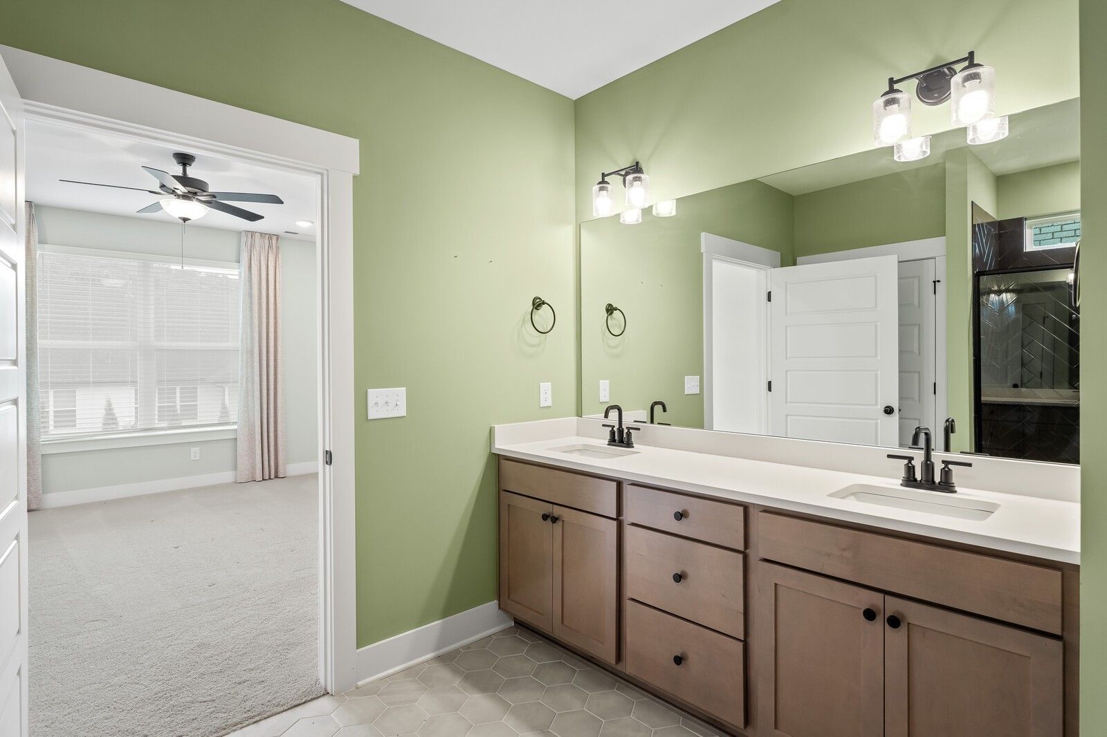 Elegant sage green bathroom with double vanity, lighted mirrors, and open doorway in Davidson Homes The Ridgeport, Gallatin, Tennessee