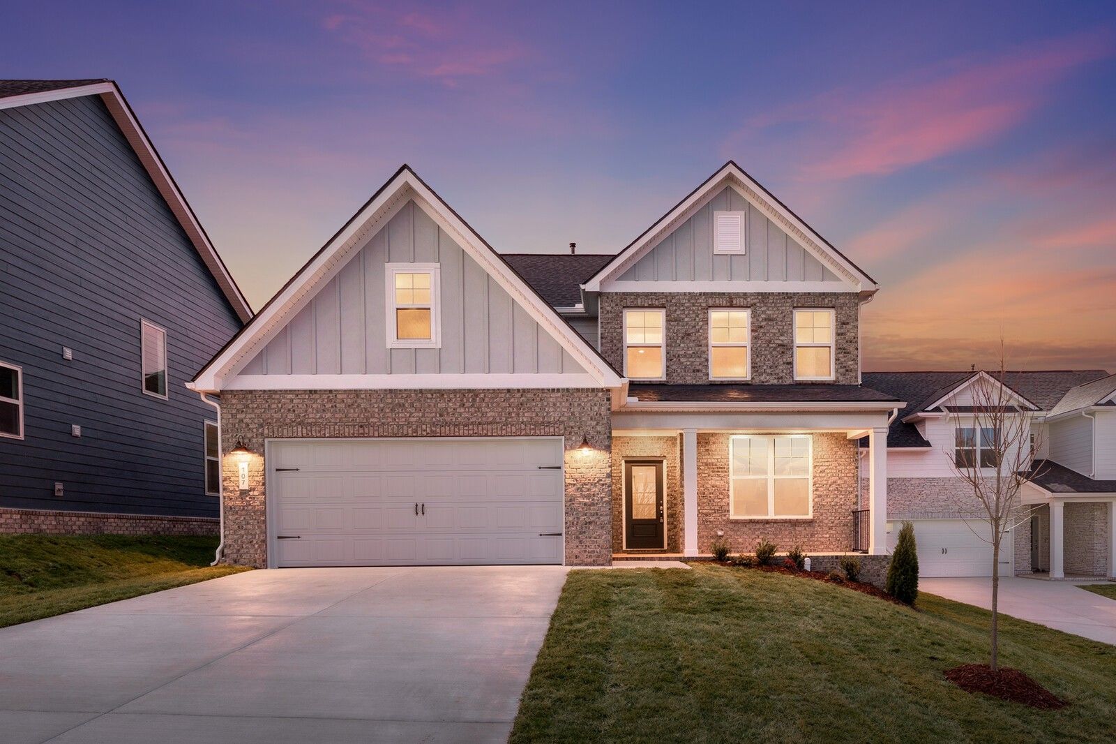 Modern 2-story brick and siding home with 2-car garage, front porch, and lush lawn at dusk in Woods Crossing, Gallatin, Tennessee