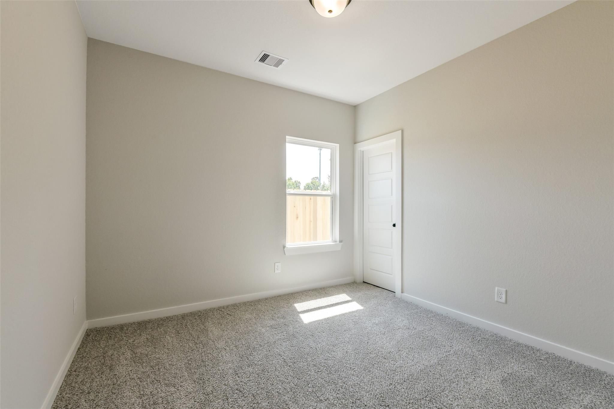 Empty secondary bedroom with beige walls, gray carpet, window and door in Davidson Homes The Daphne H, Sundance Cove, Crosby, Texas
