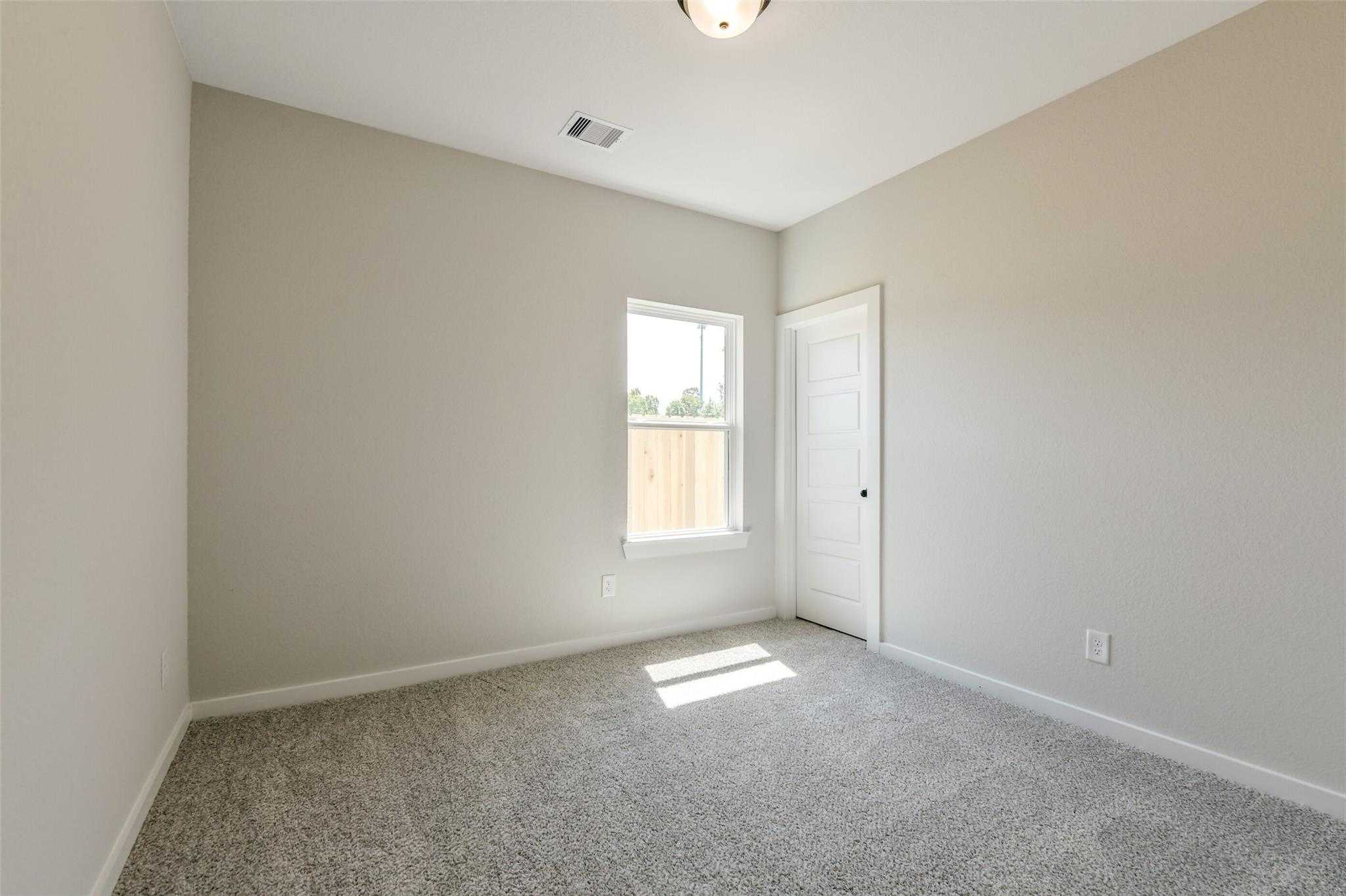 Empty secondary bedroom with beige walls, gray carpet, window and door in Davidson Homes The Daphne H, Sundance Cove, Crosby, Texas