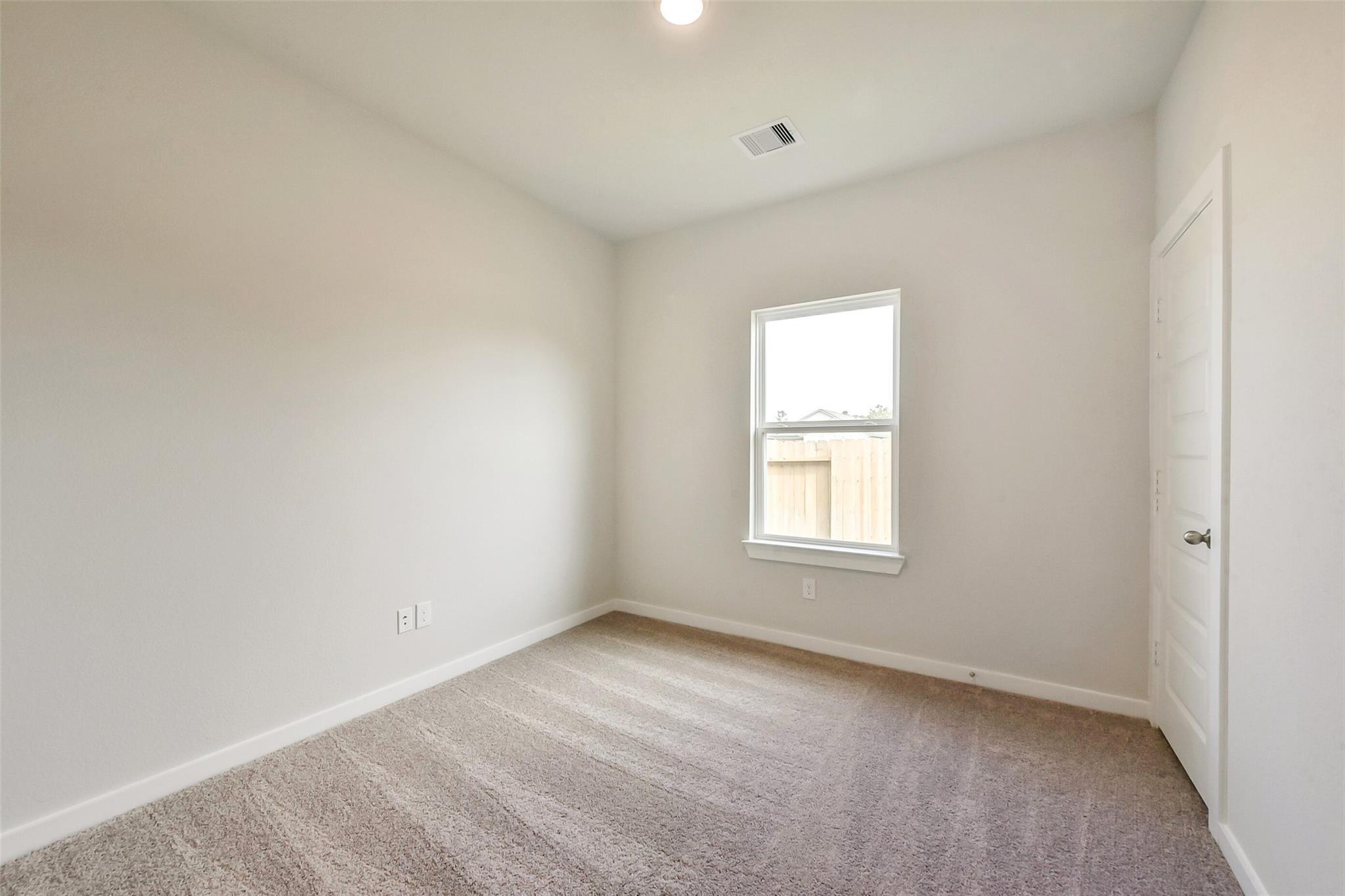 Spacious secondary bedroom with beige walls, carpet flooring, large window to backyard fence in The Comal G, Dayton Texas