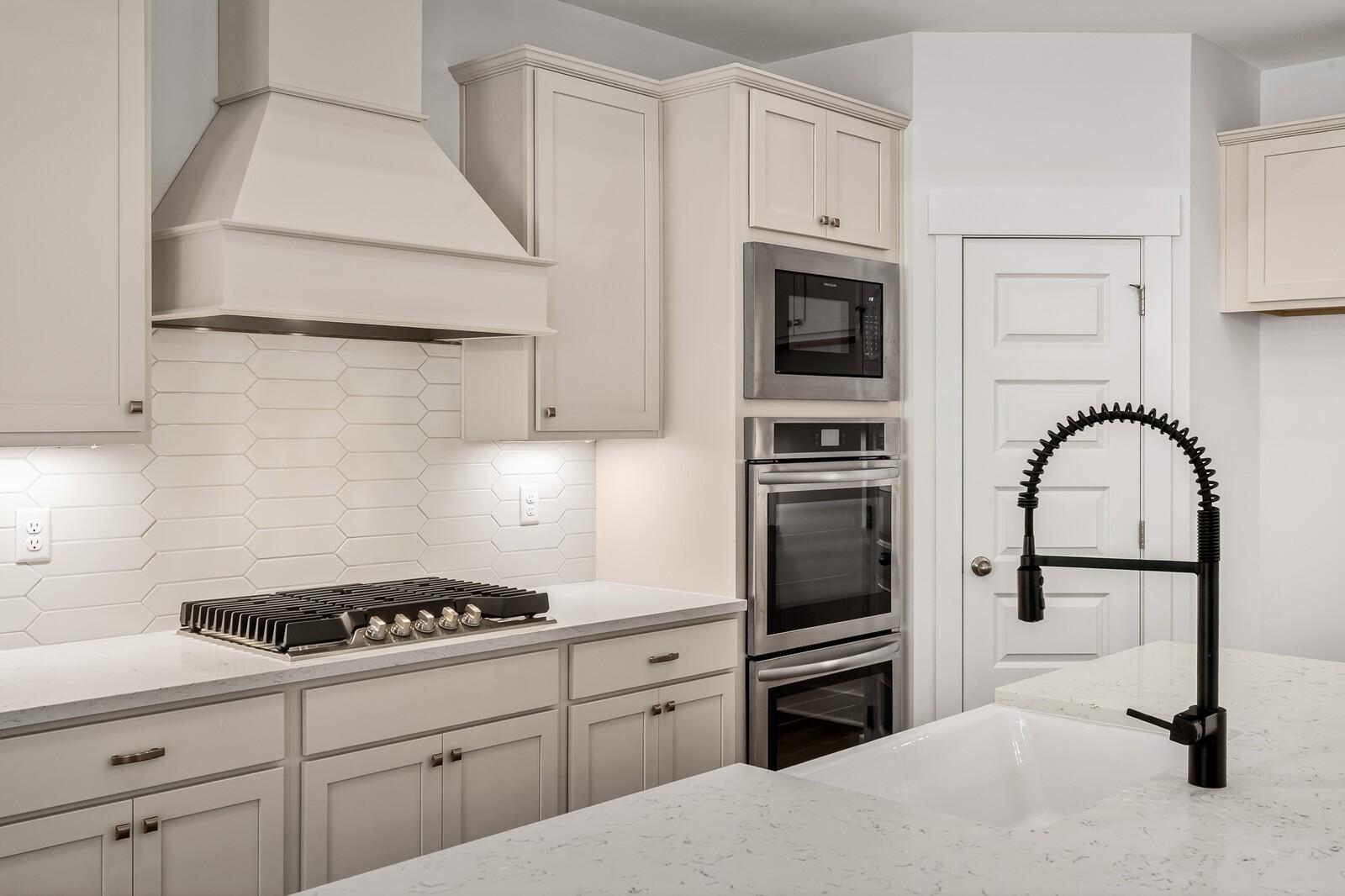 Modern white kitchen with shaker cabinets, quartz counters, gas range, double ovens, subway tile backsplash, and black faucet in Ridgeport C home, Gallatin, TN
