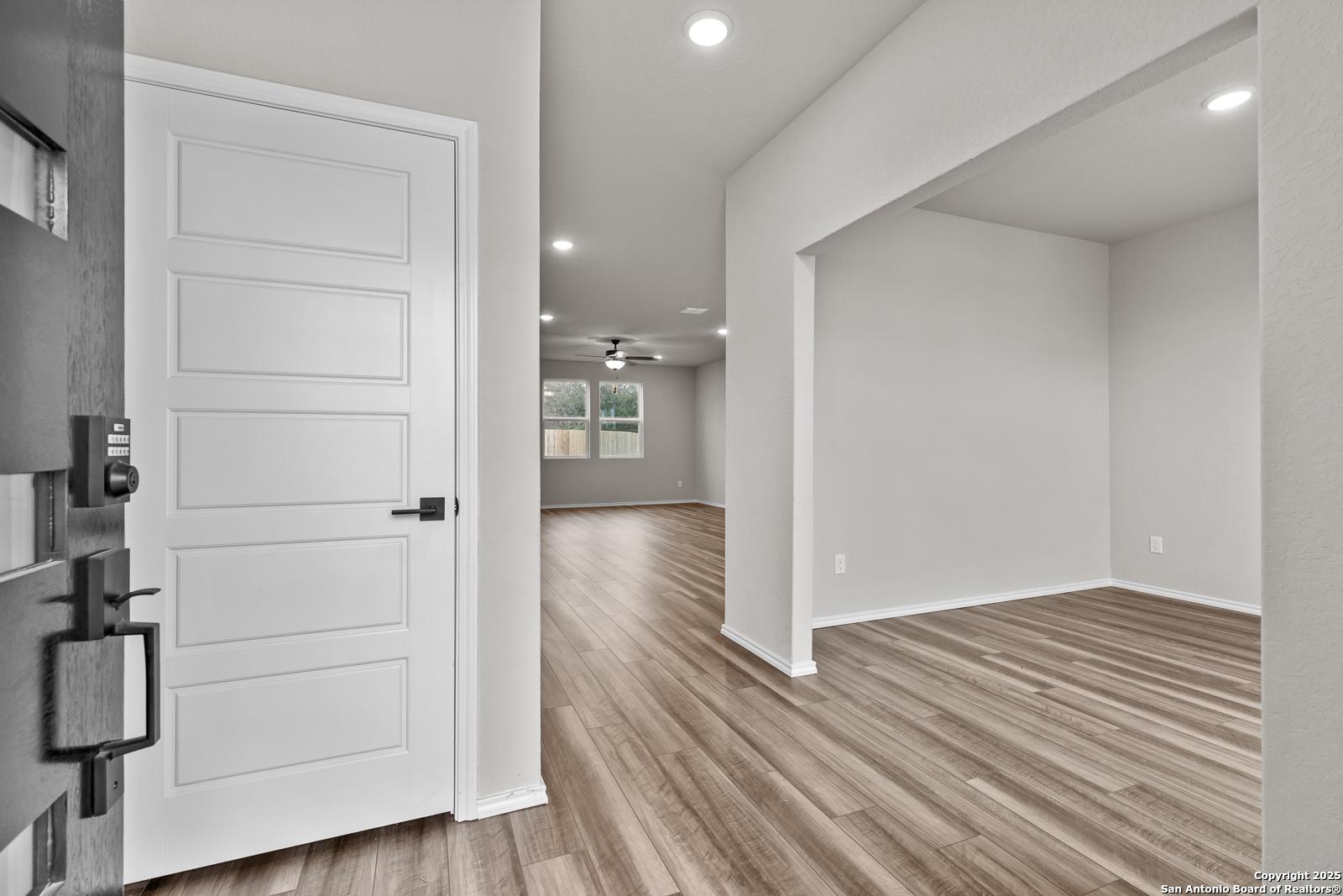 Bright entry hallway with white paneled door, light wood floors, recessed lights in Davidson Homes The Murray I, San Antonio