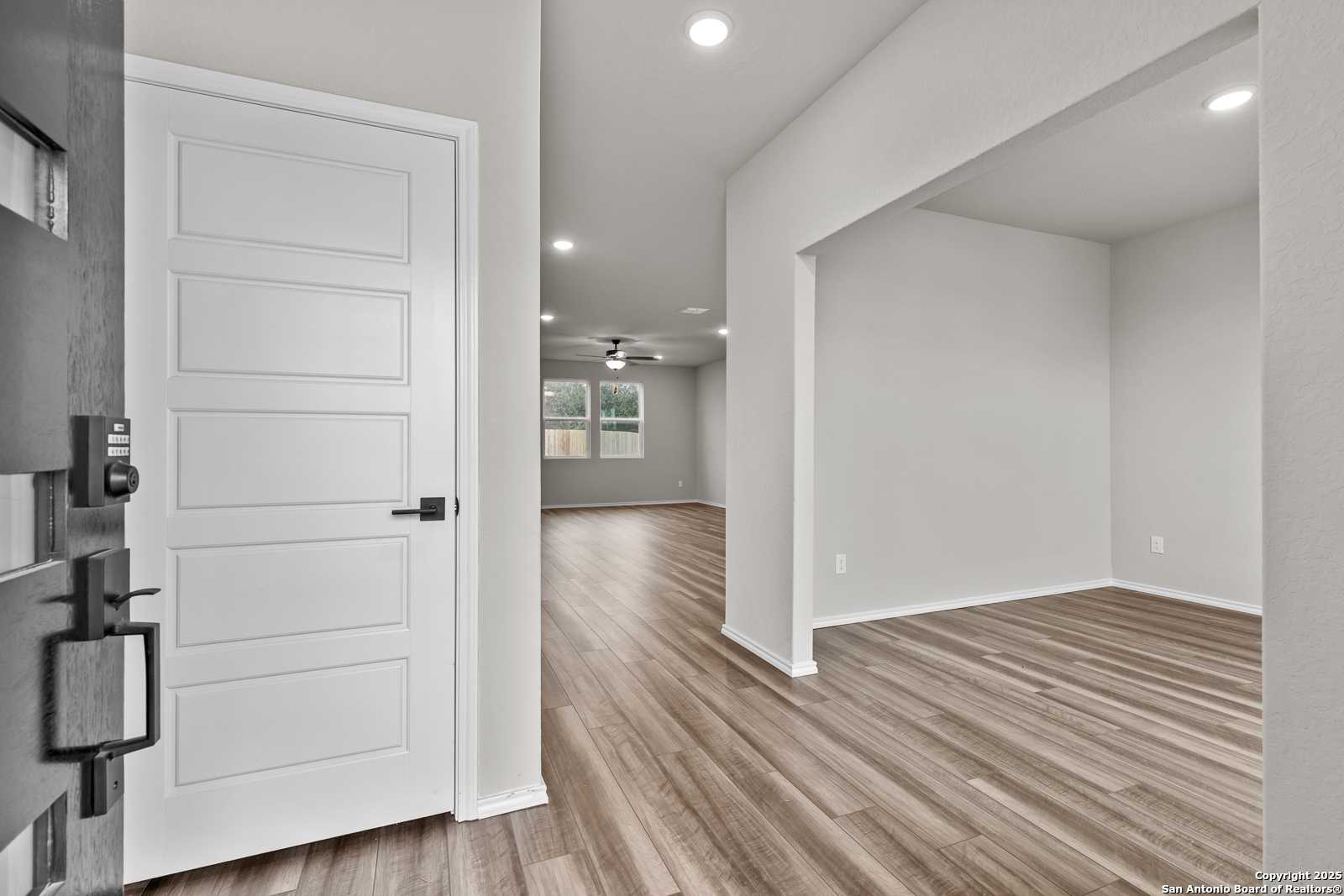 Bright entry hallway with white paneled door, light wood floors, recessed lights in Davidson Homes The Murray I, San Antonio