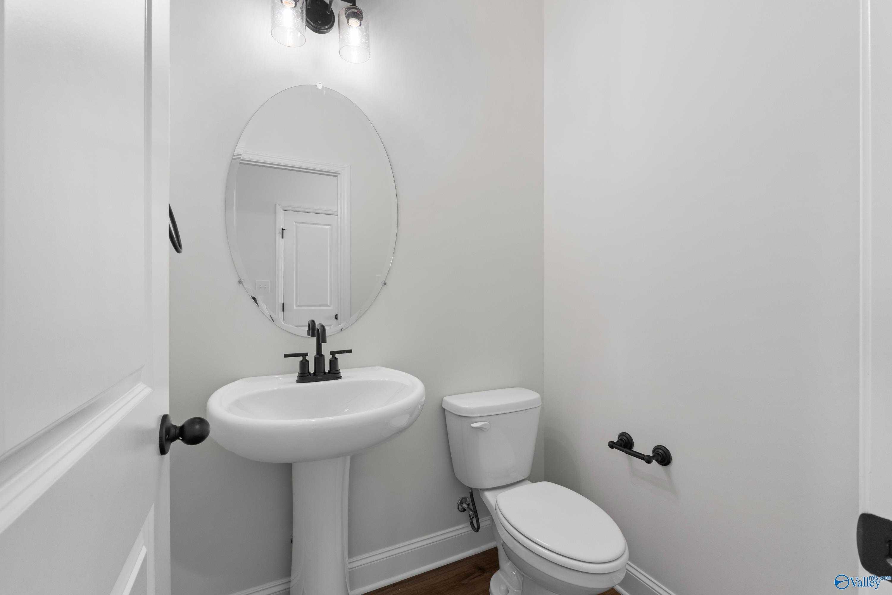 Elegant powder room with pedestal sink, round mirror, black fixtures in Davidson Homes The Rockford B, Toney, Alabama